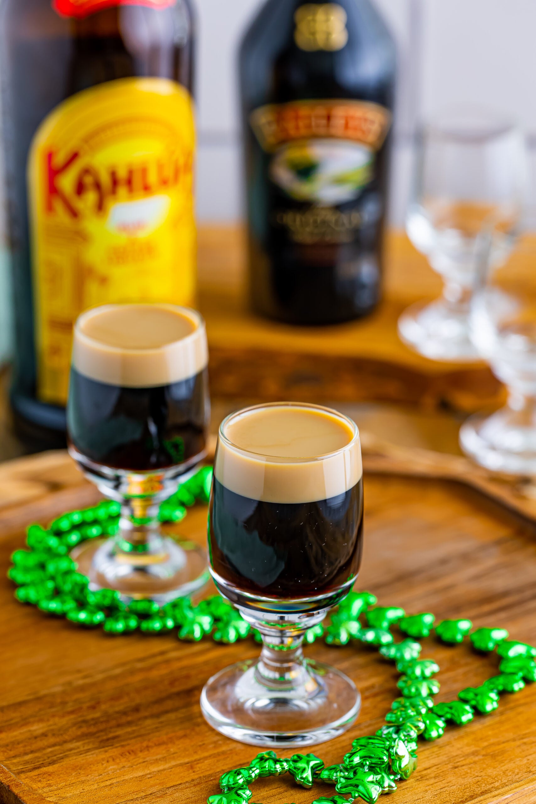 Two Baby Guinness Shots on a wooden board with a green shamrock necklace. 