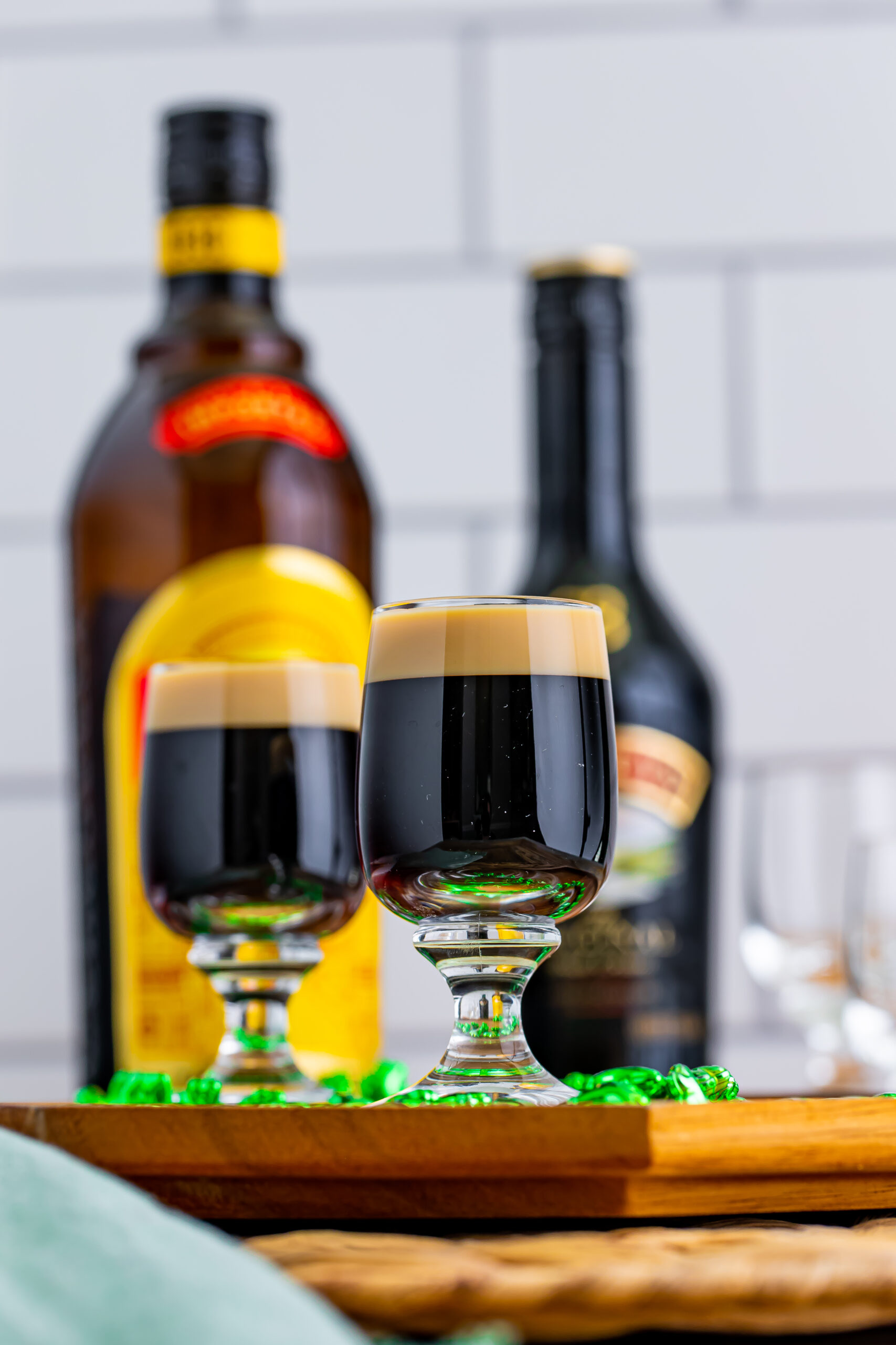 Two Baby Guinness Shots on a wooden board with a green shamrock necklace. 