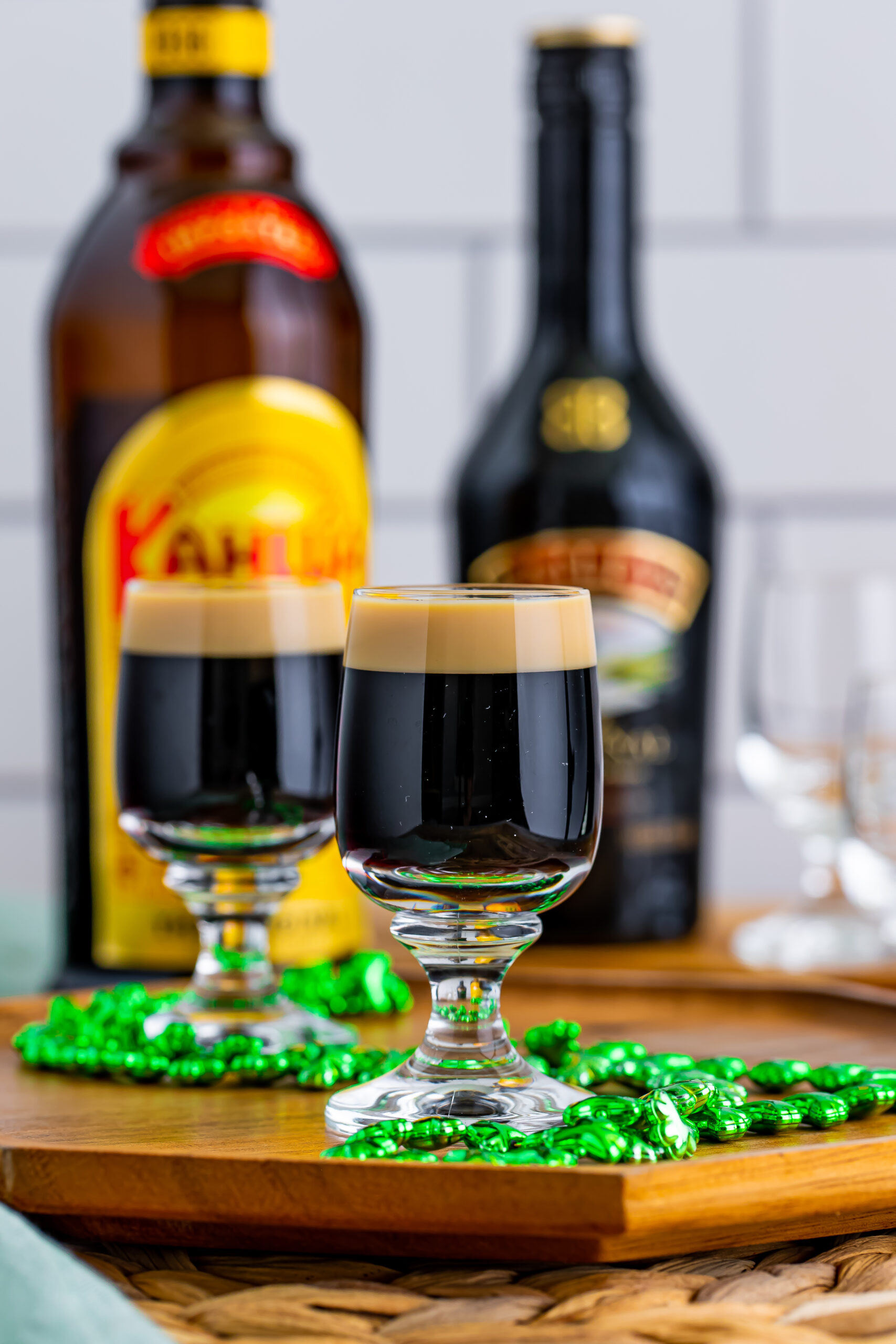 Two Baby Guinness Shots on a wooden board with a green shamrock necklace. 