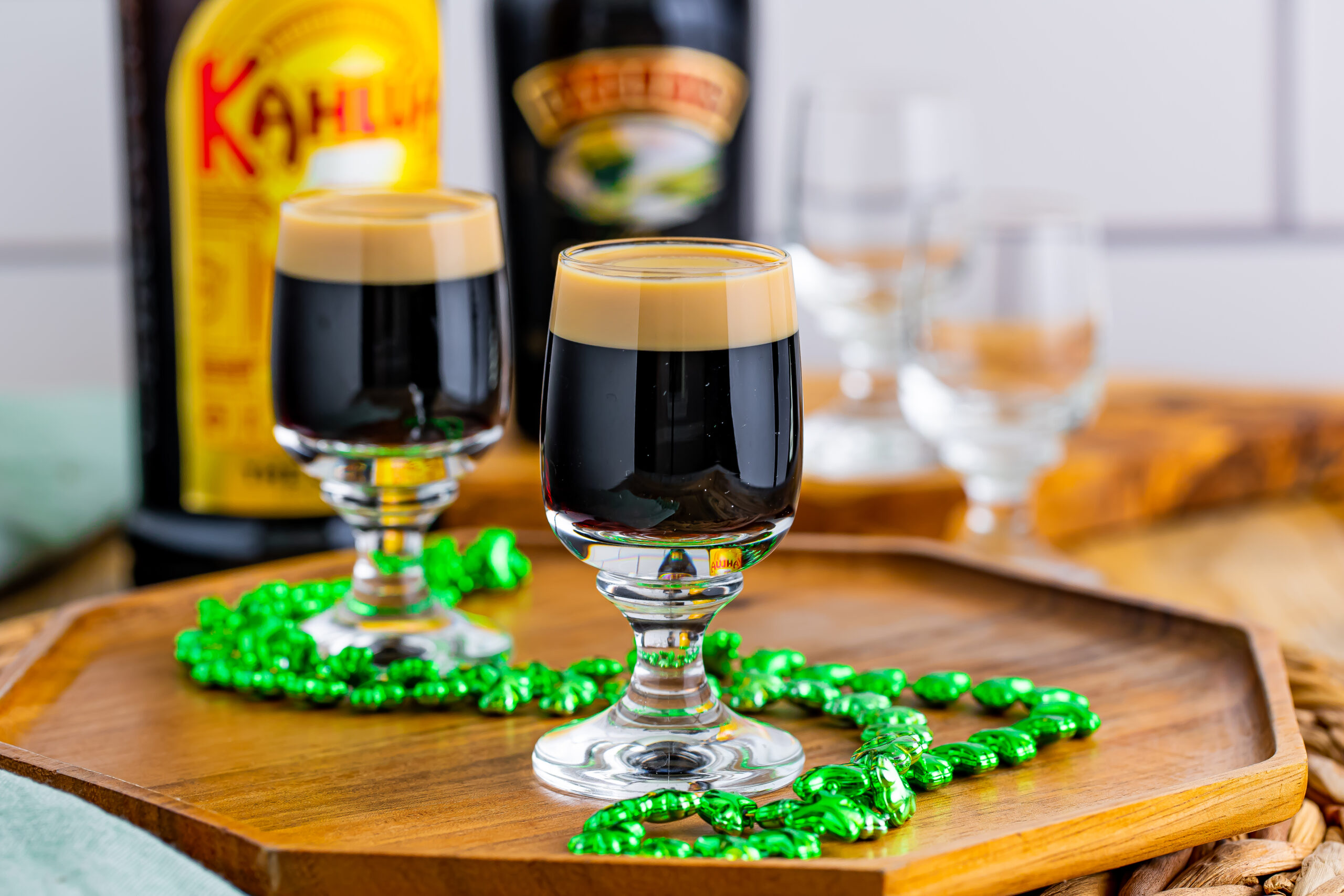 Two Baby Guinness Shots on a wooden board with a green shamrock necklace. 