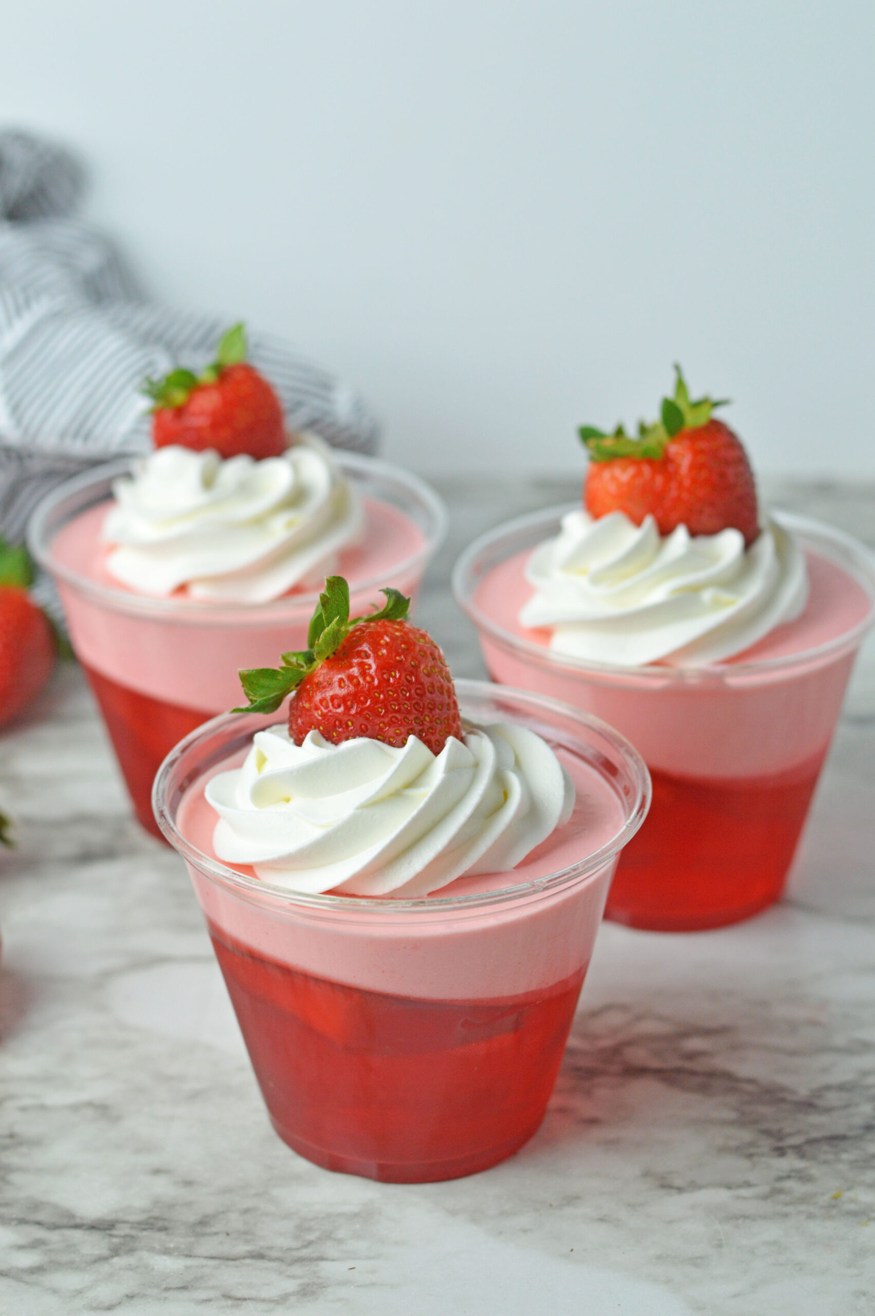 Front view of Strawberry Jello Parfait in plastic cups topped with whipped cream and a strawberry.