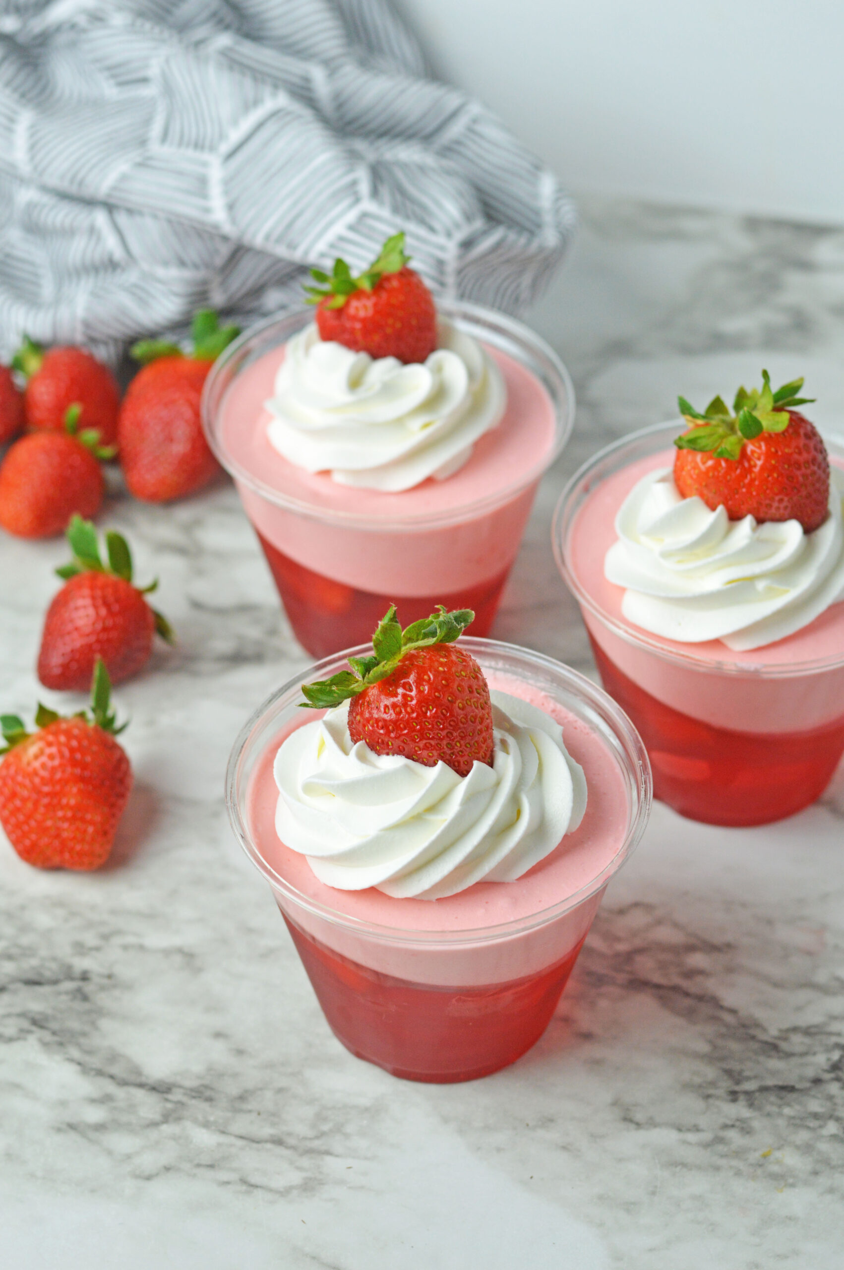 Front view of Strawberry Jello Parfait in plastic cups topped with whipped cream and a strawberry.