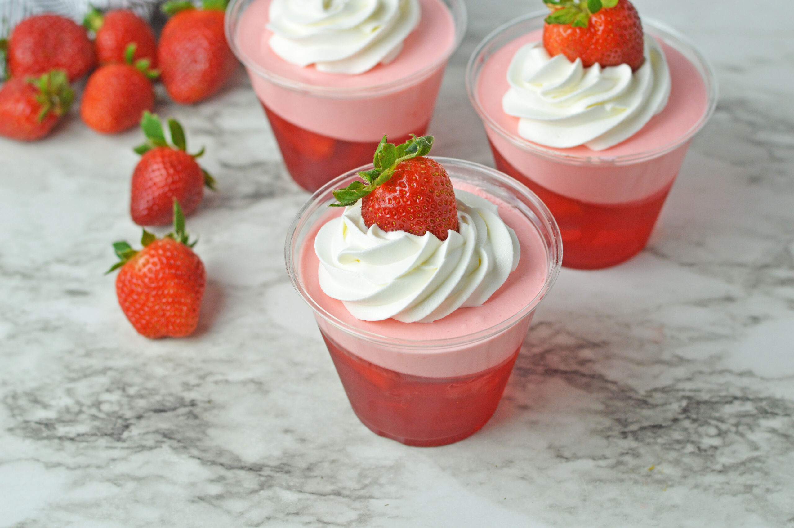 Front view of Strawberry Jello Parfait in plastic cups topped with whipped cream and a strawberry.