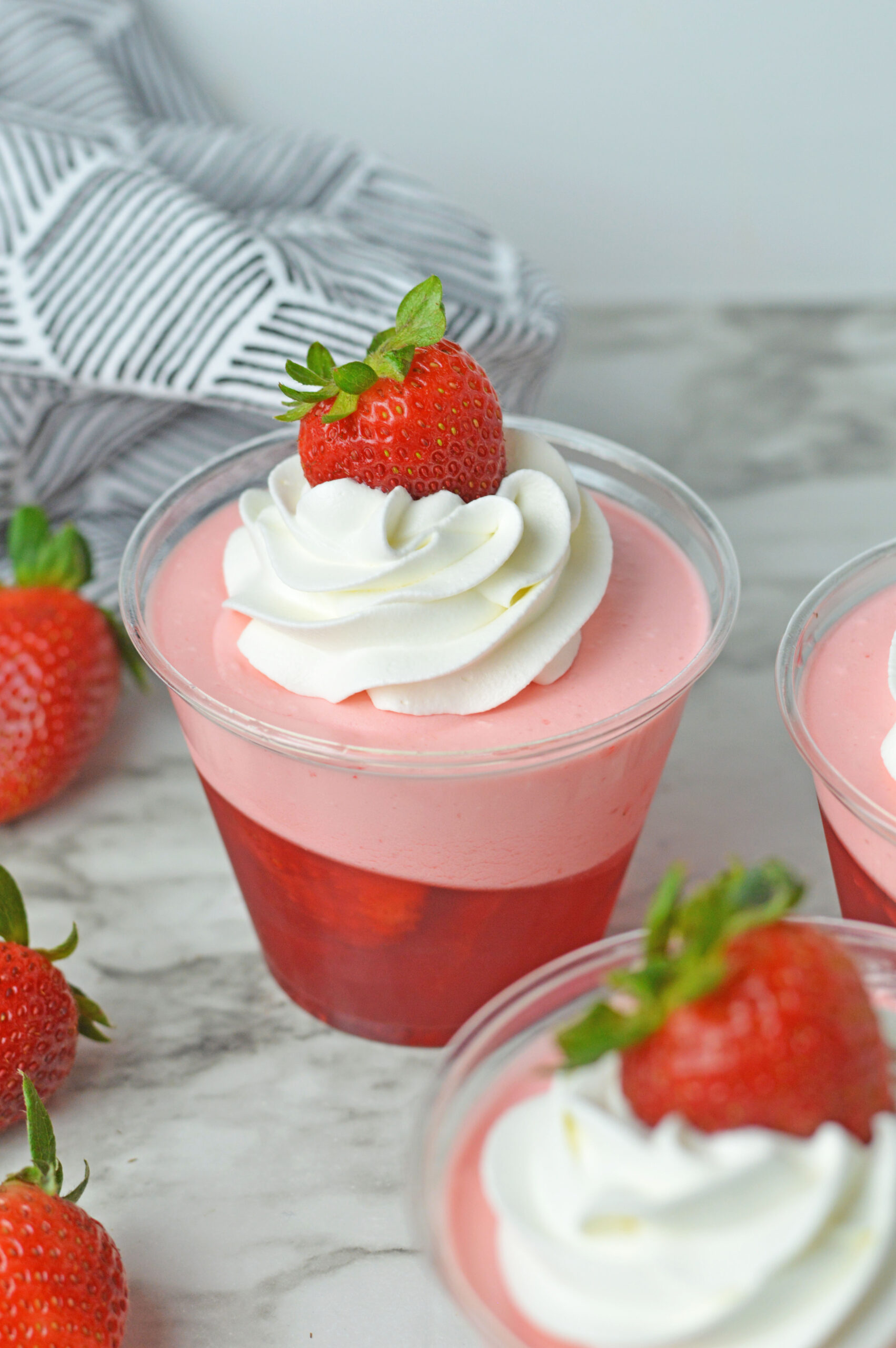 Close up view of Strawberry Jello Parfait in plastic cups topped with whipped cream and a strawberry.