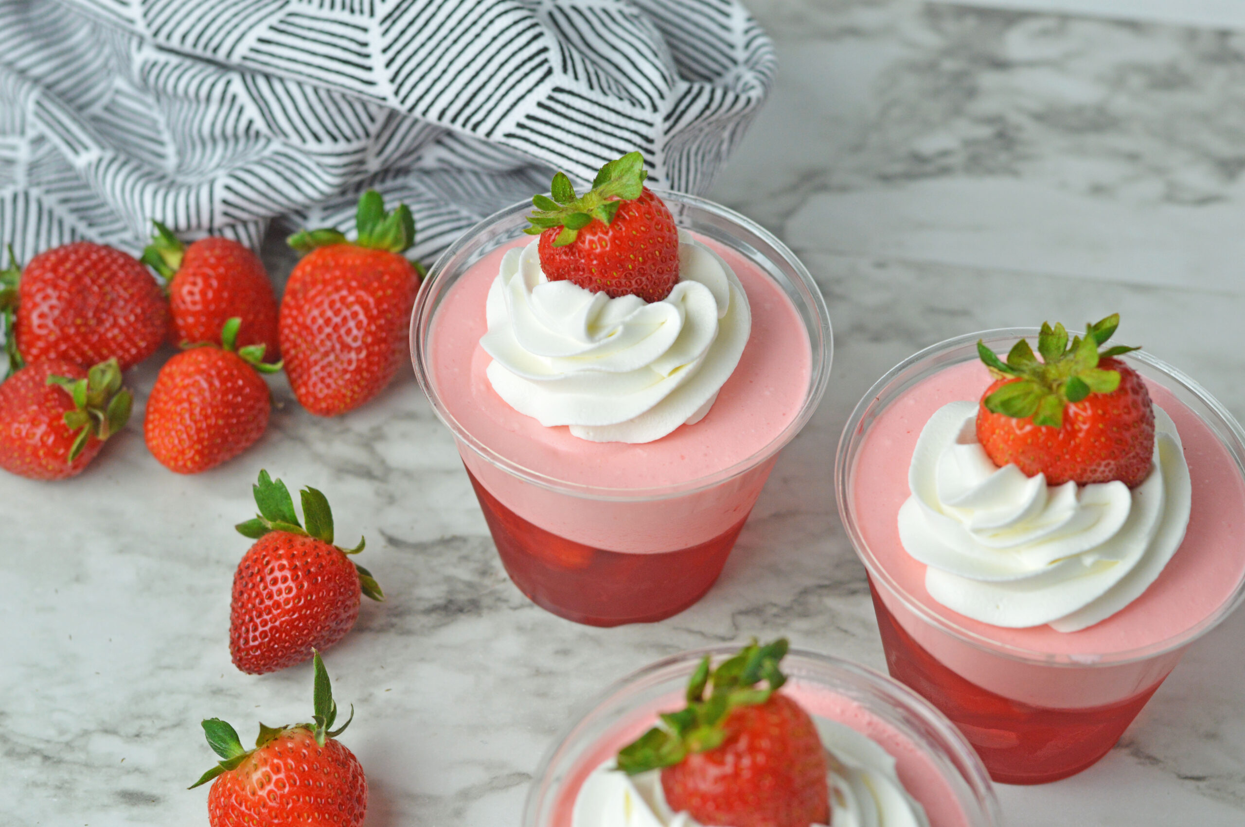 Overhead view of Strawberry Jello Parfait in plastic cups topped with whipped cream and a strawberry.