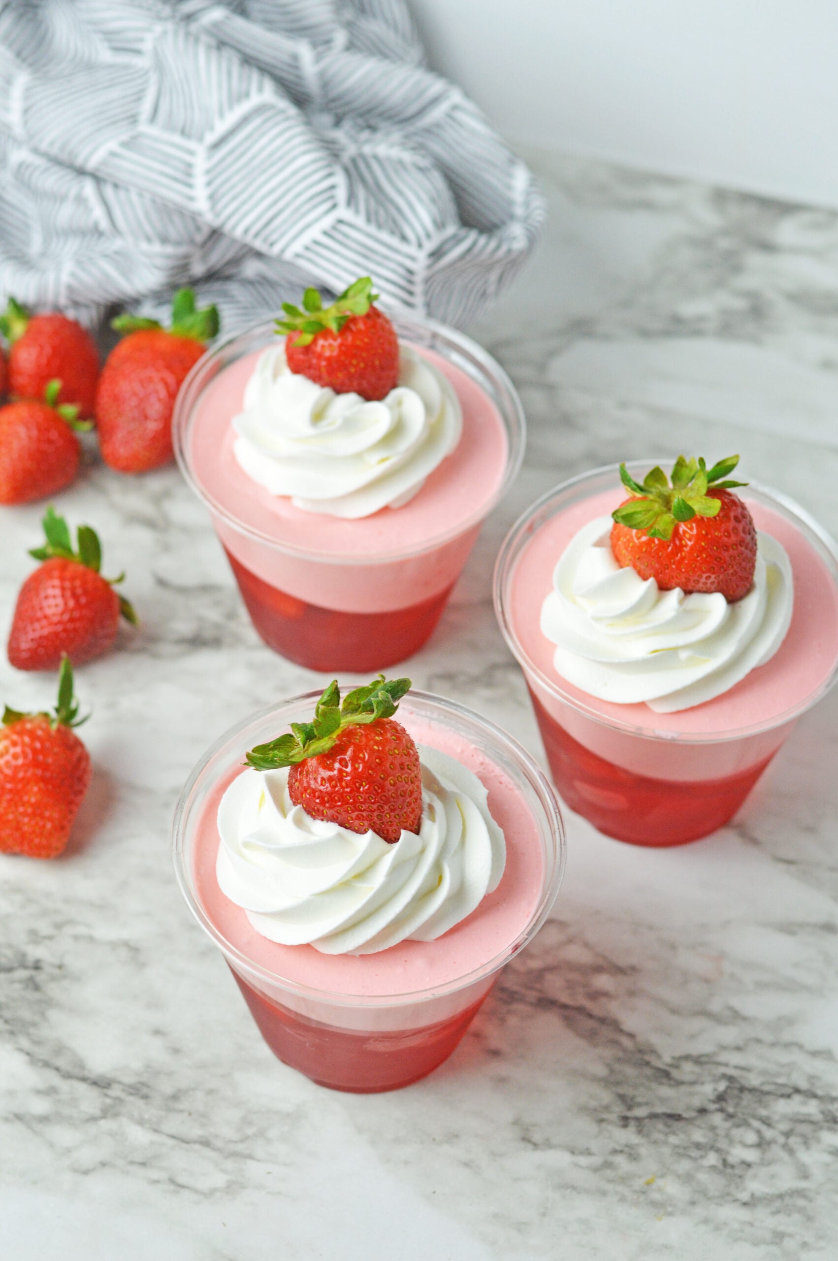 Overhead view of Strawberry Jello Parfait in plastic cups topped with whipped cream and a strawberry.