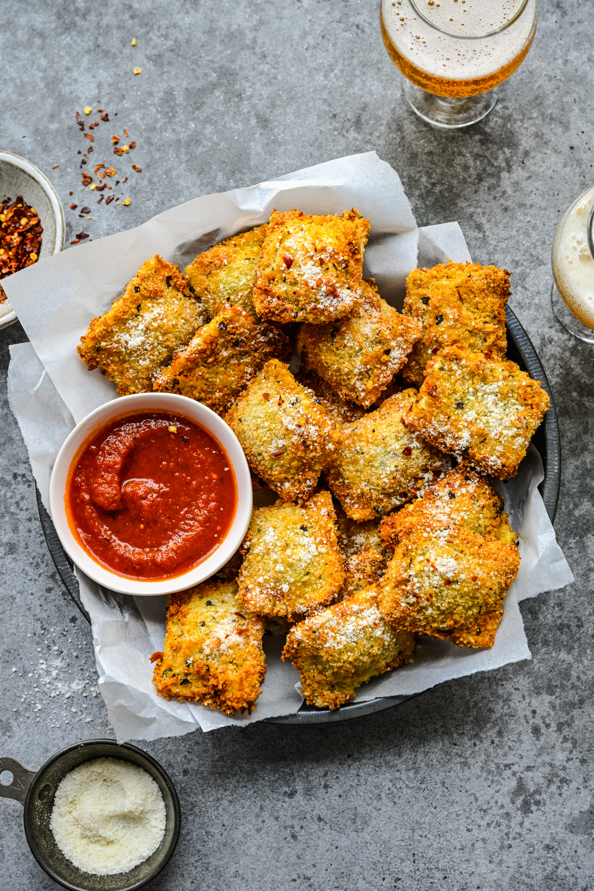 Overhead view of Air Fryer Ravioli in a black serving tray with parchment paper and marinara sauce.