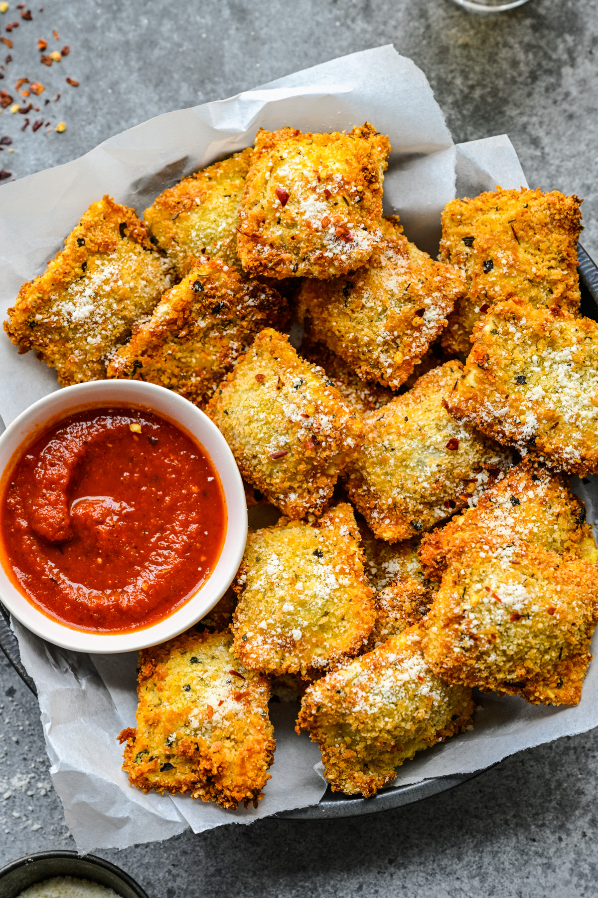 Overhead view of Air Fryer Ravioli in a black serving tray with parchment paper and marinara sauce.