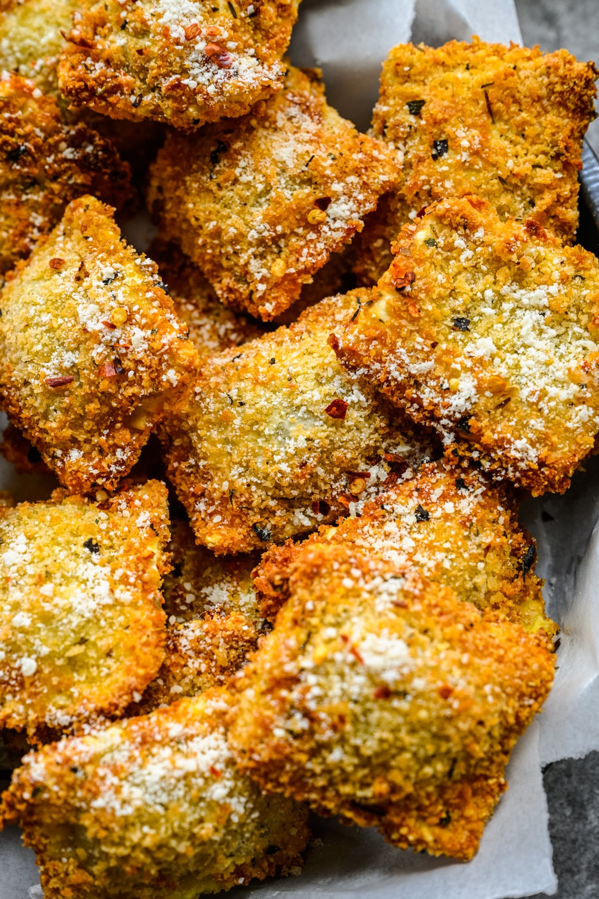 Close up overhead view of Air Fryer Ravioli in a black serving tray with parchment paper and marinara sauce.