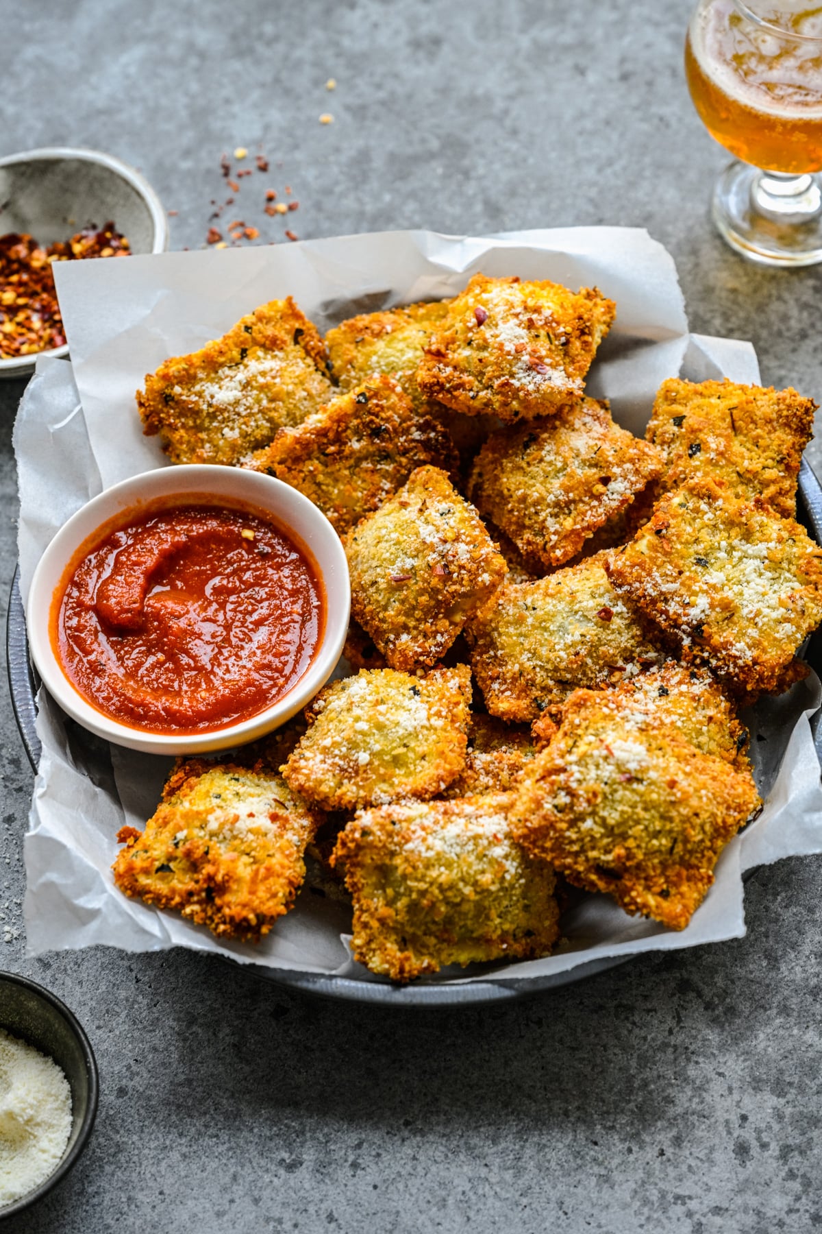 Side view of Air Fryer Ravioli in a black serving tray with parchment paper and marinara sauce.