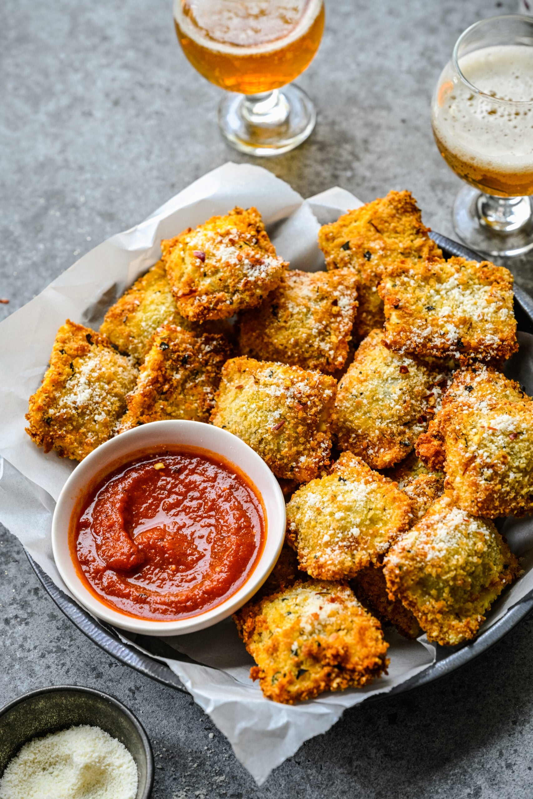 Close up view of Air Fryer Ravioli in a black serving tray with parchment paper and a side of marinara sauce.