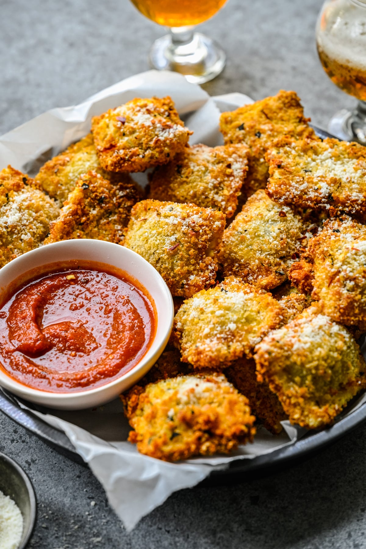 Side view of Air Fryer Ravioli in a black serving tray with parchment paper and marinara sauce.