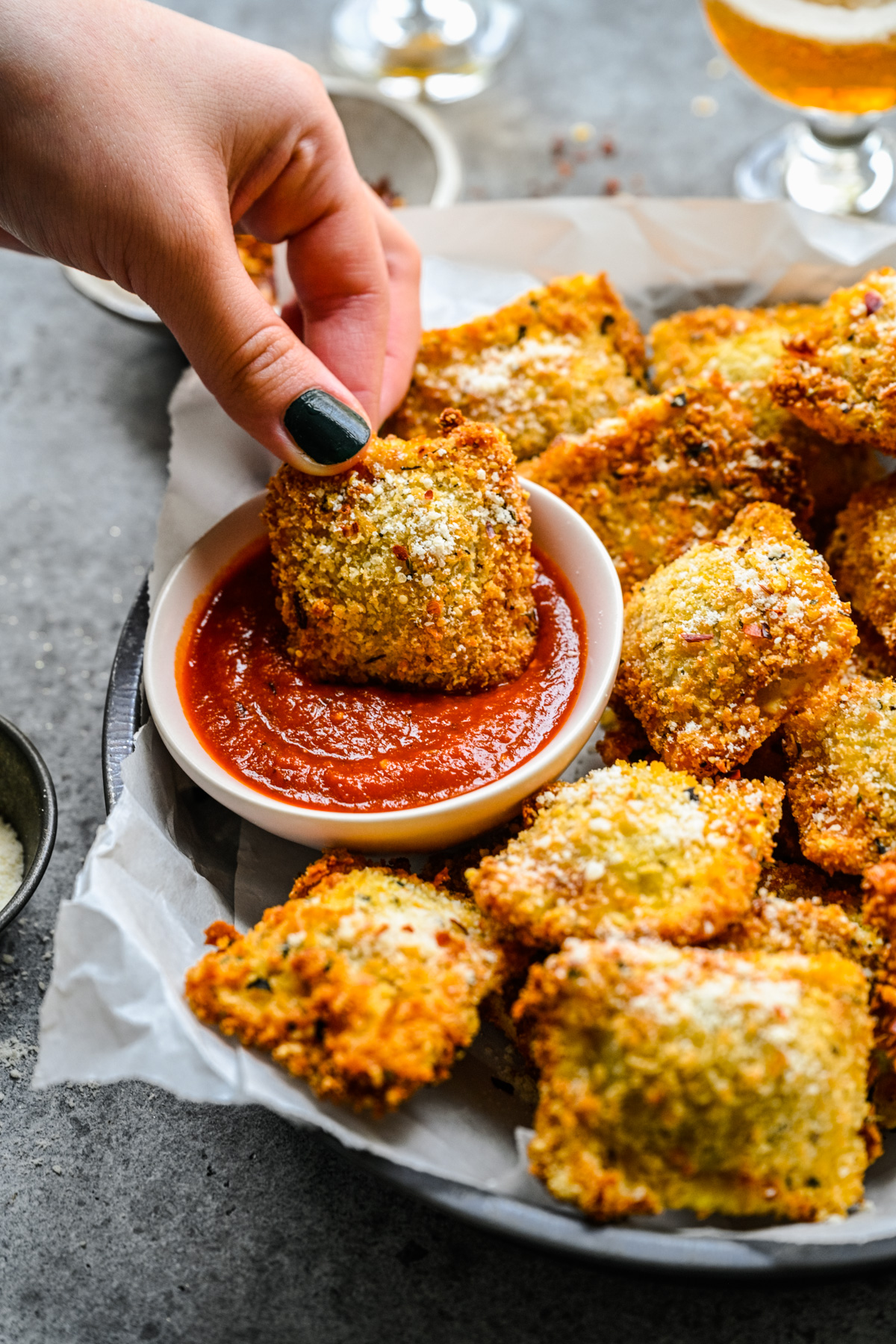 A hand dipping an air fryer ravioli into marinara sauce.