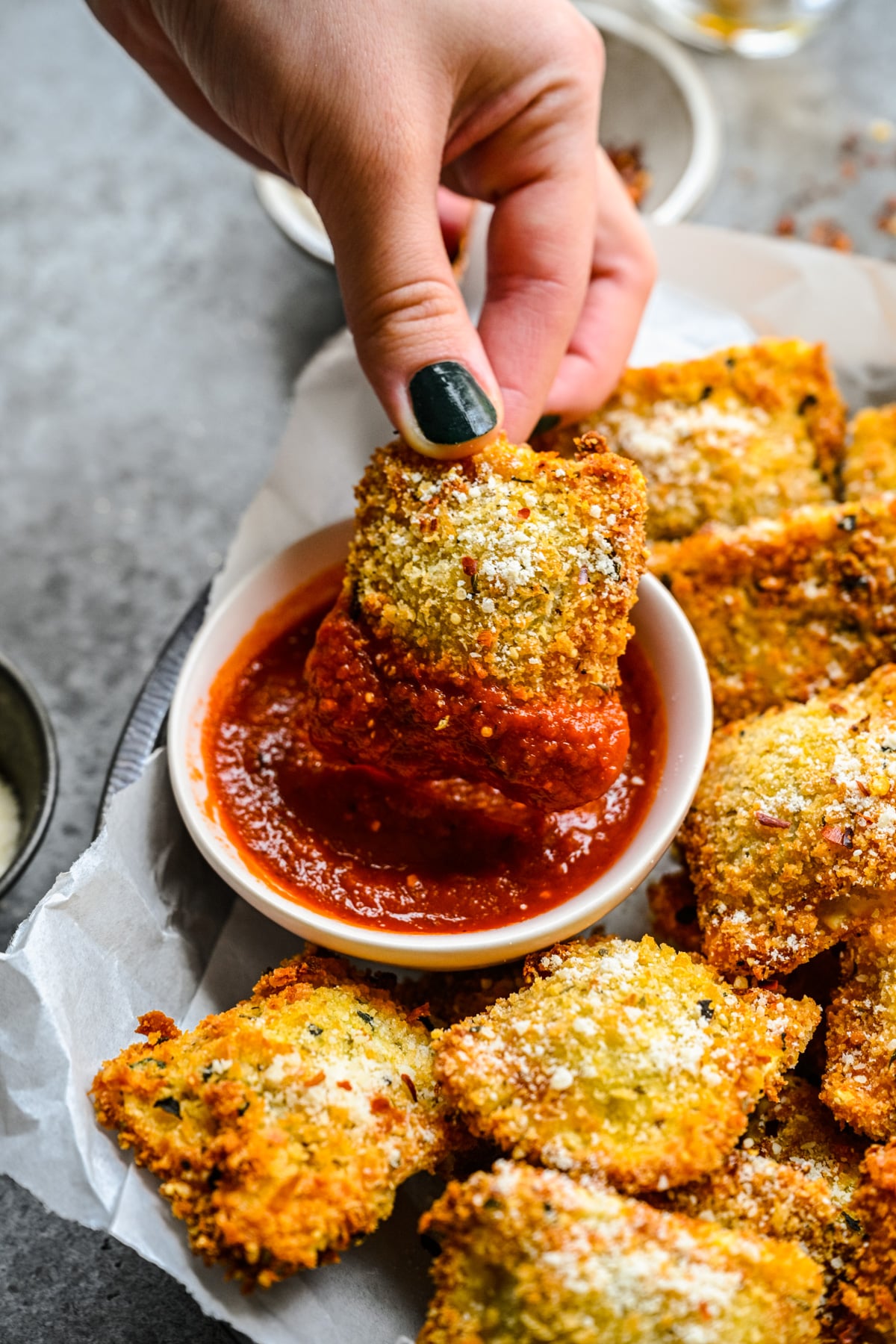 A hand dipping an air fryer ravioli into marinara sauce.