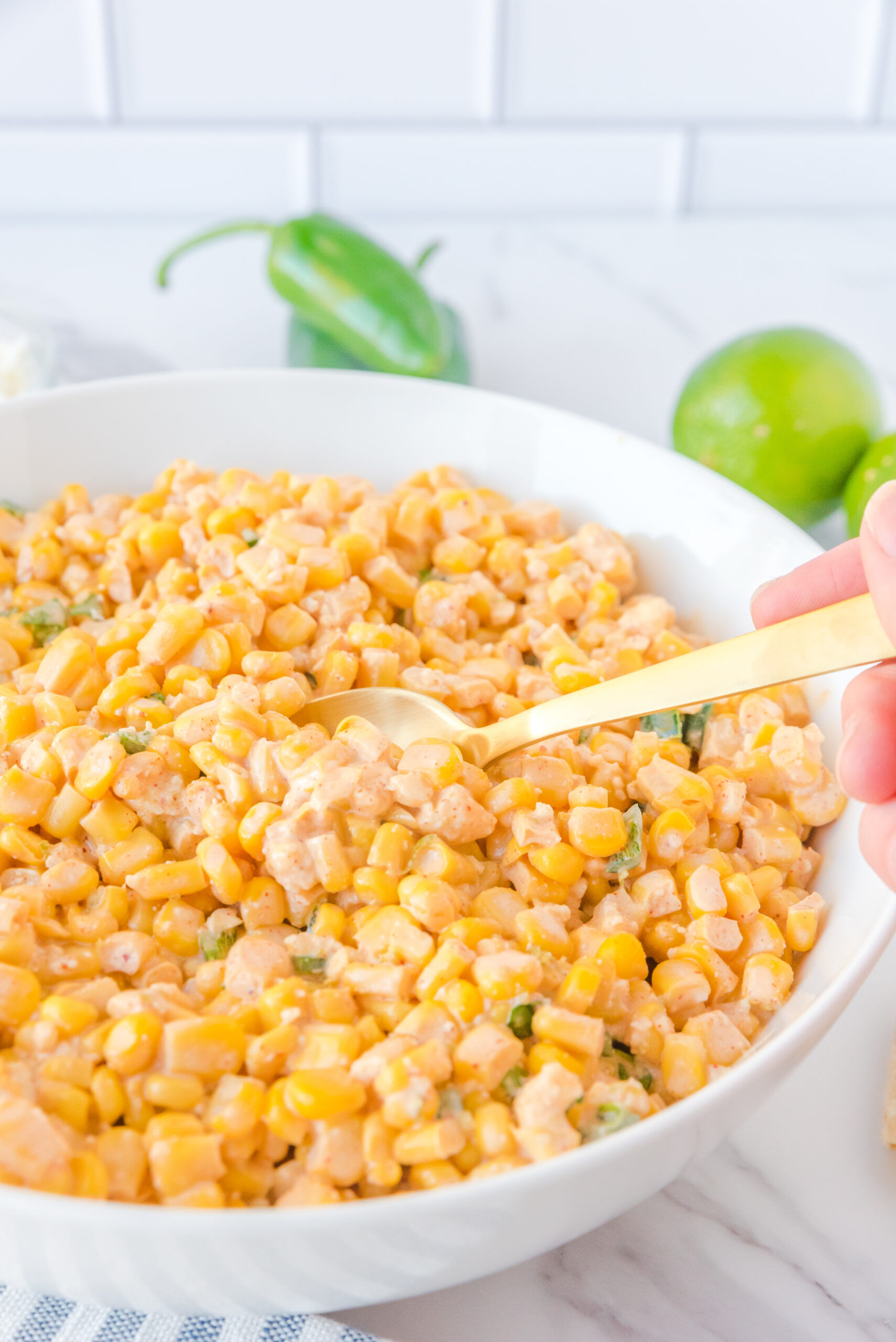 A gold spoon removing Mexican Street Corn Salad from a large white serving bowl.
