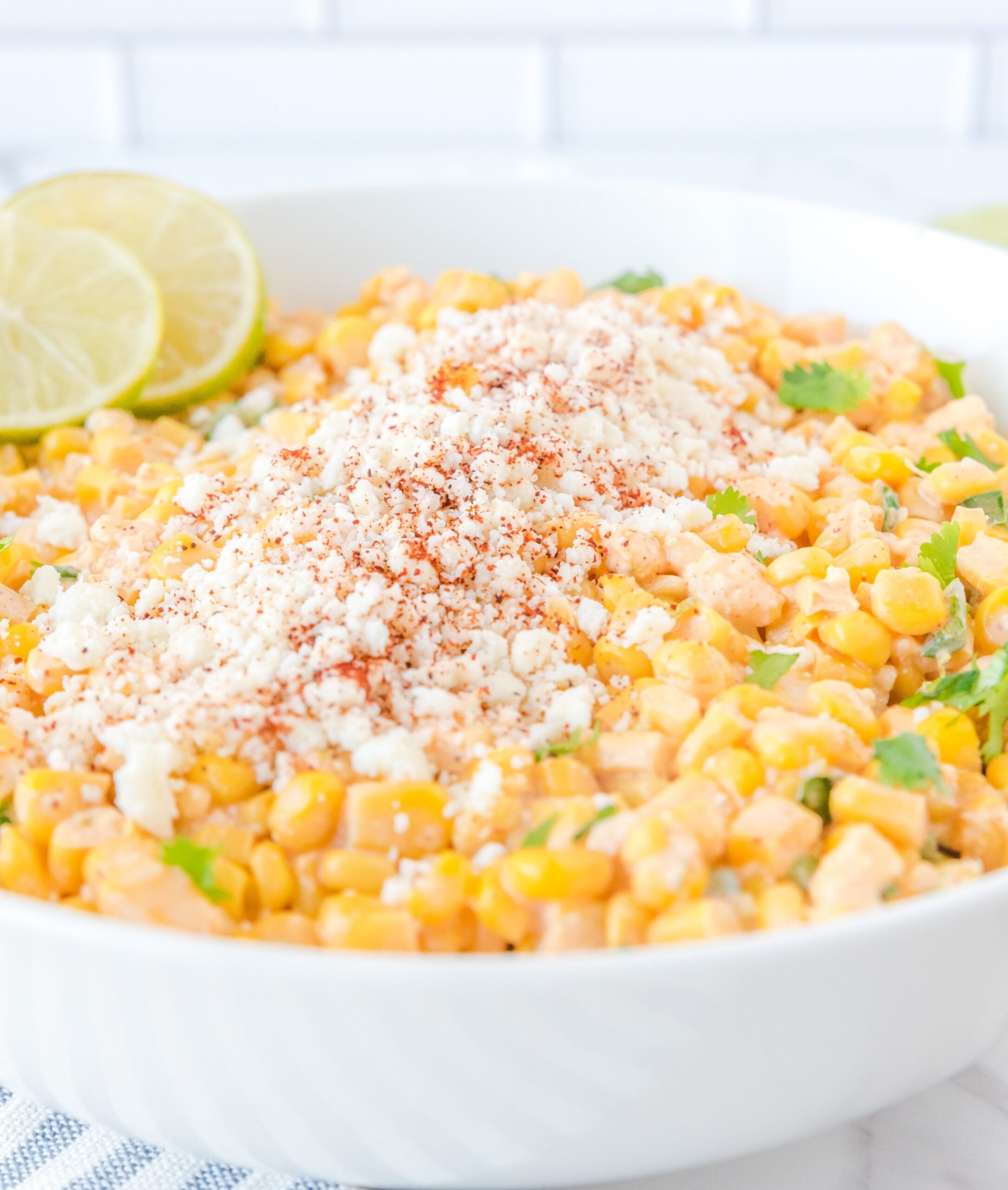 Up close shot of Mexican Street Corn Salad in a large white serving bowl, topped with feta cheese and sliced limes.