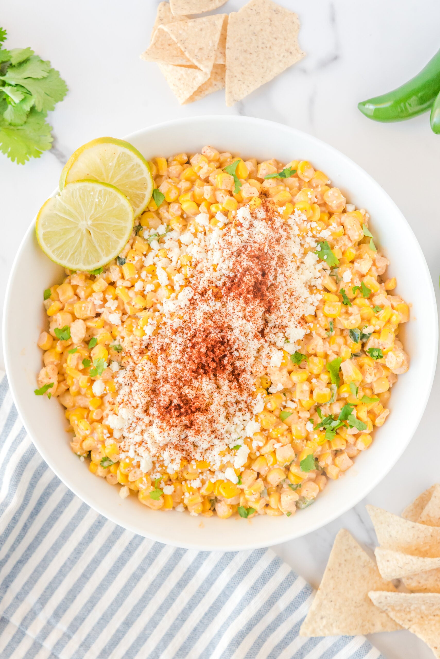 Mexican Street Corn Salad in a large white bowl topped with paprika and fresh lime slices.