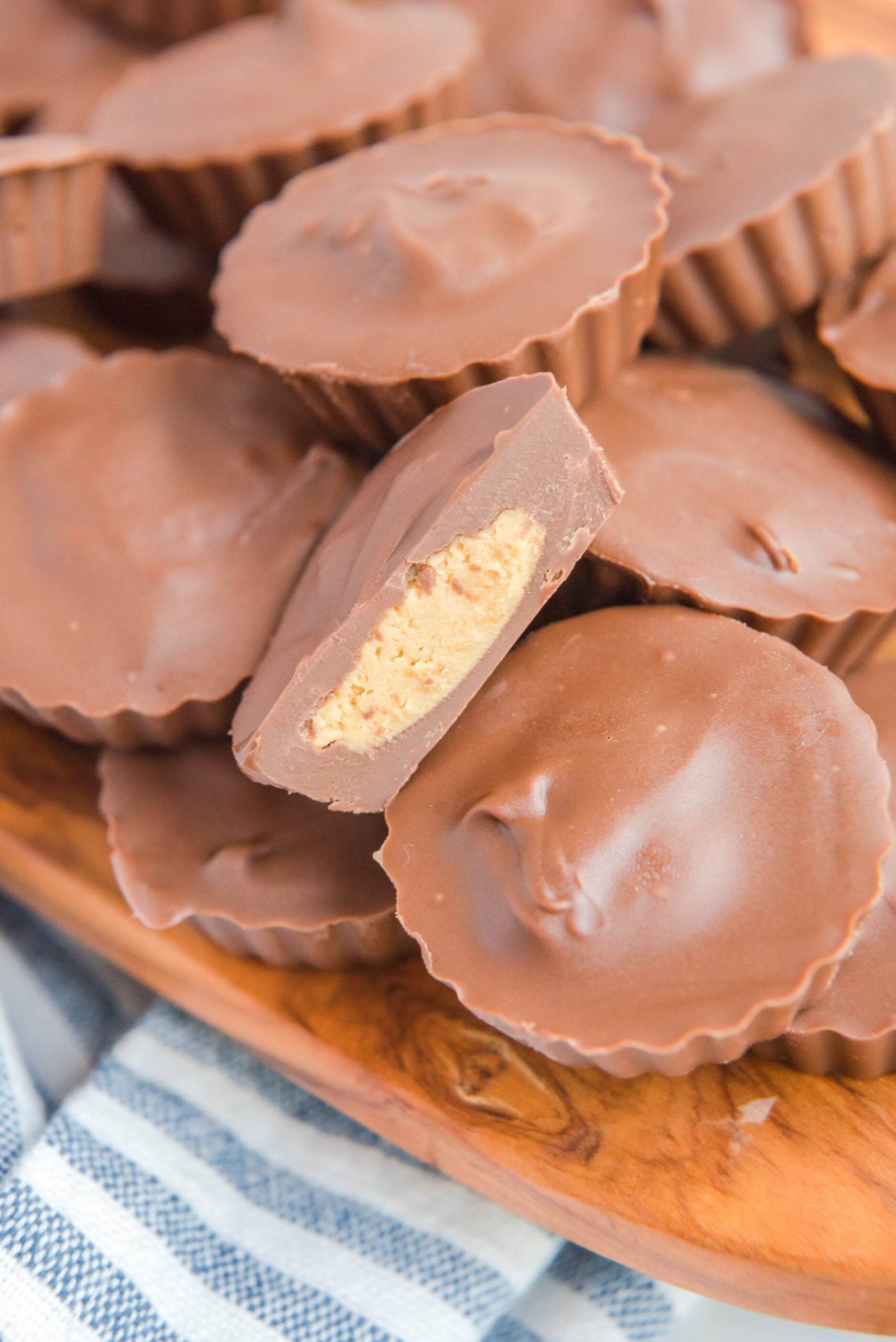 Homemade Reese's Peanut Butter Cups stacked on a wooden serving board with a bite removed from one to show the filling.