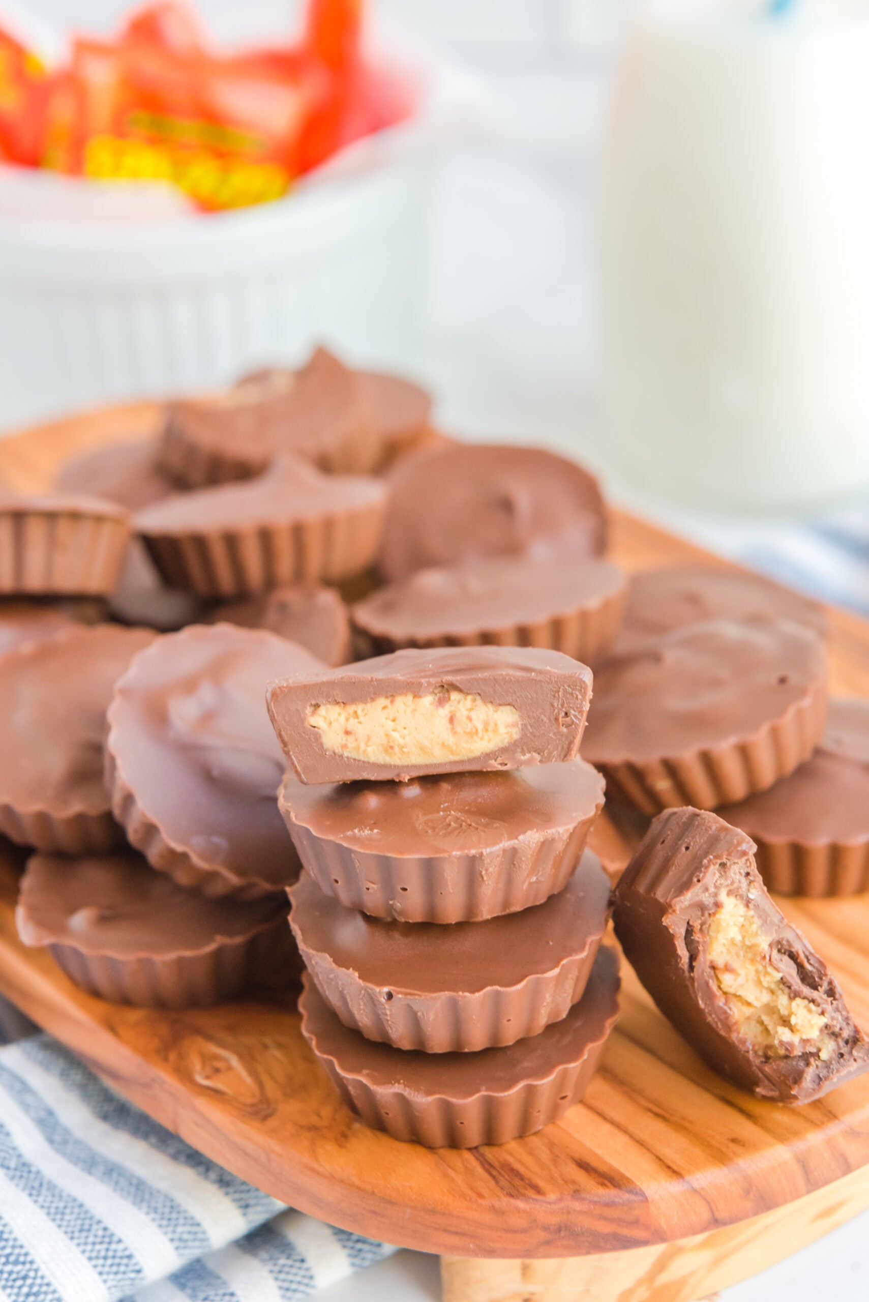 Homemade Reese's Peanut Butter Cups stacked on a wooden serving board with a bite removed from one to show the filling.