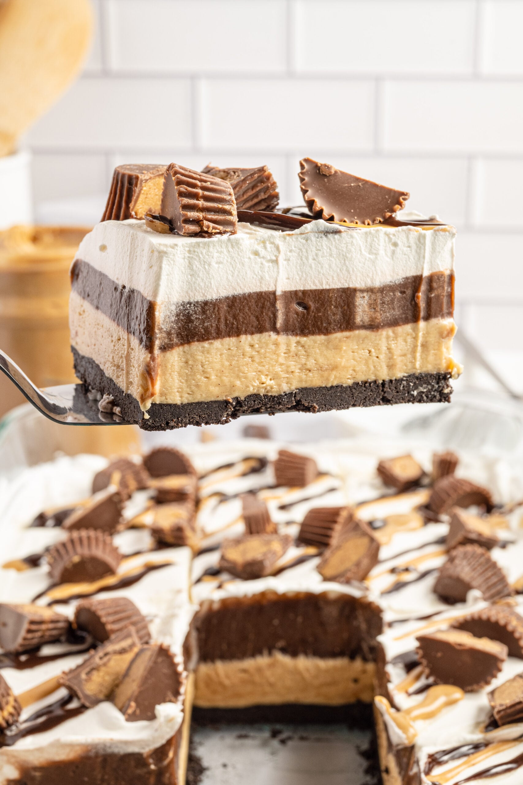 A piece of Reese's chocolate peanut butter cup lasagna being removed from the baking dish with a silver spatula. 