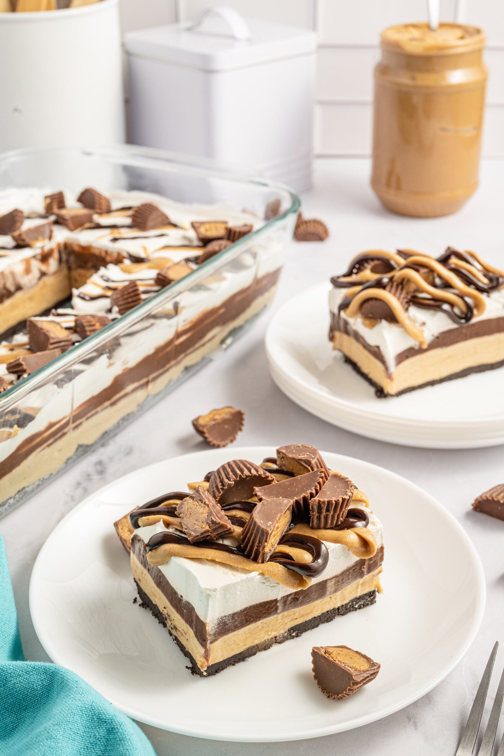 Two pieces of chocolate peanut butter lasagna on two white plates with Reese's cups in the background. 