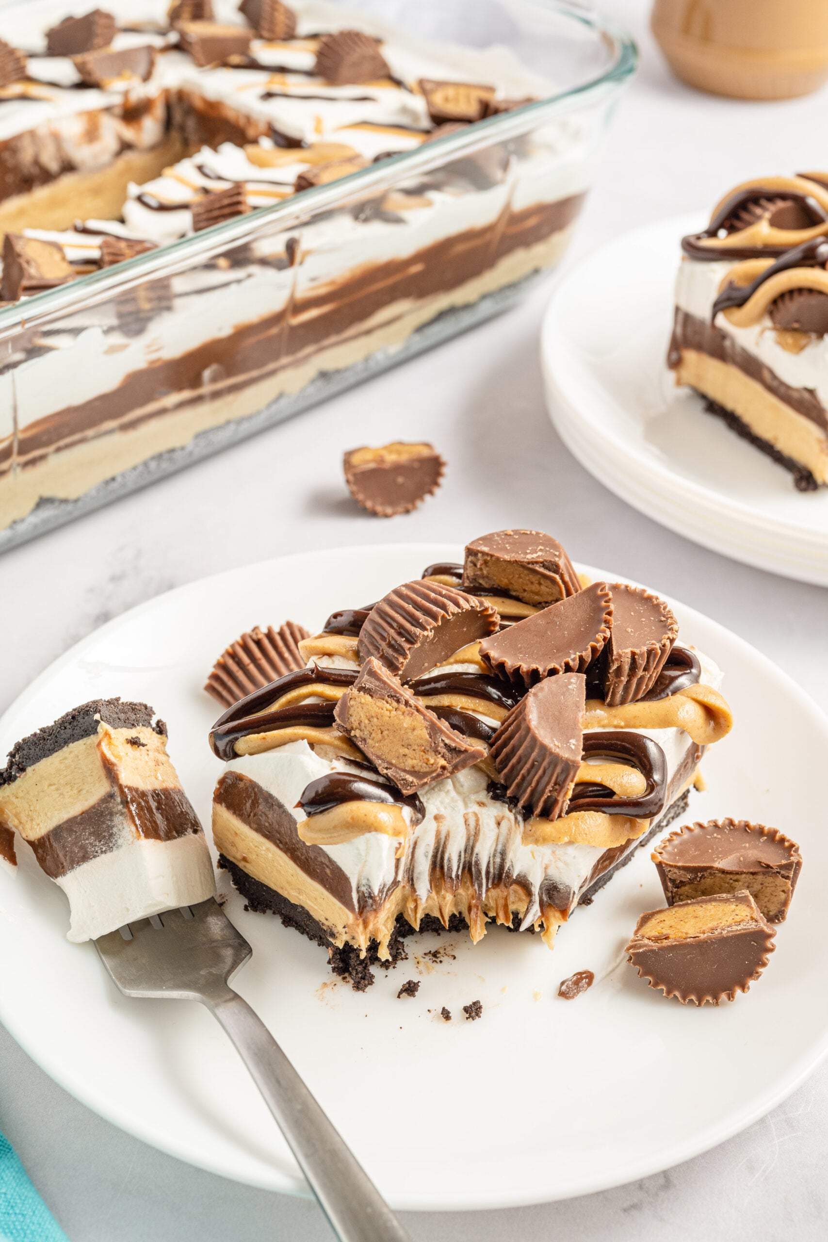 Two pieces of chocolate peanut butter lasagna on two white plates with Reese's cups in the background. 