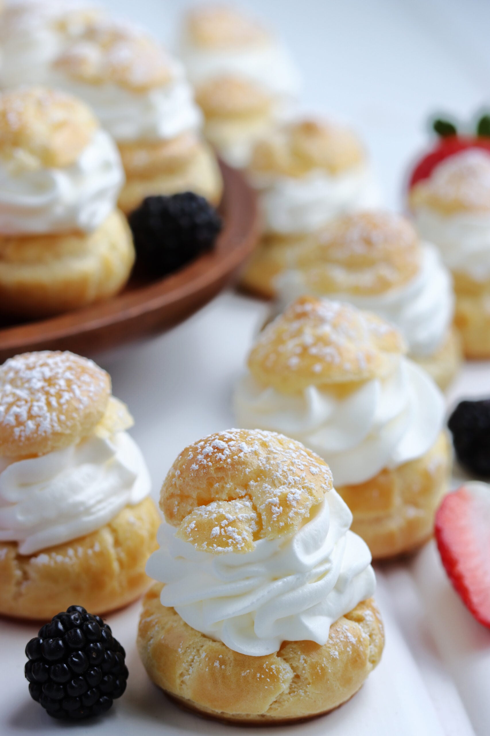 Cream puffs sprinkled with powdered sugar with fresh berries in the background. 