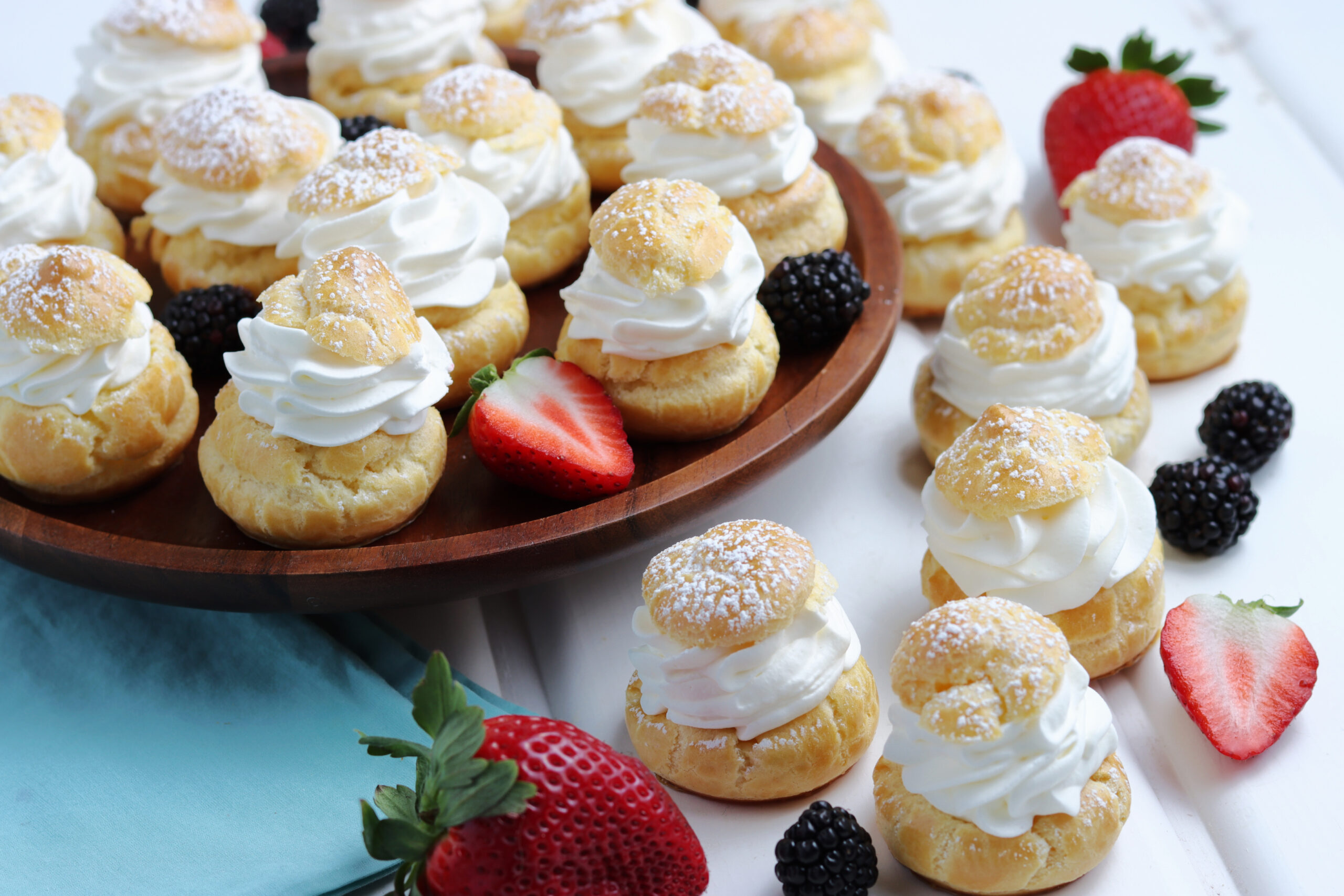 Overhead shot of Cream puffs sprinkled with powdered sugar with fresh berries in the background. 