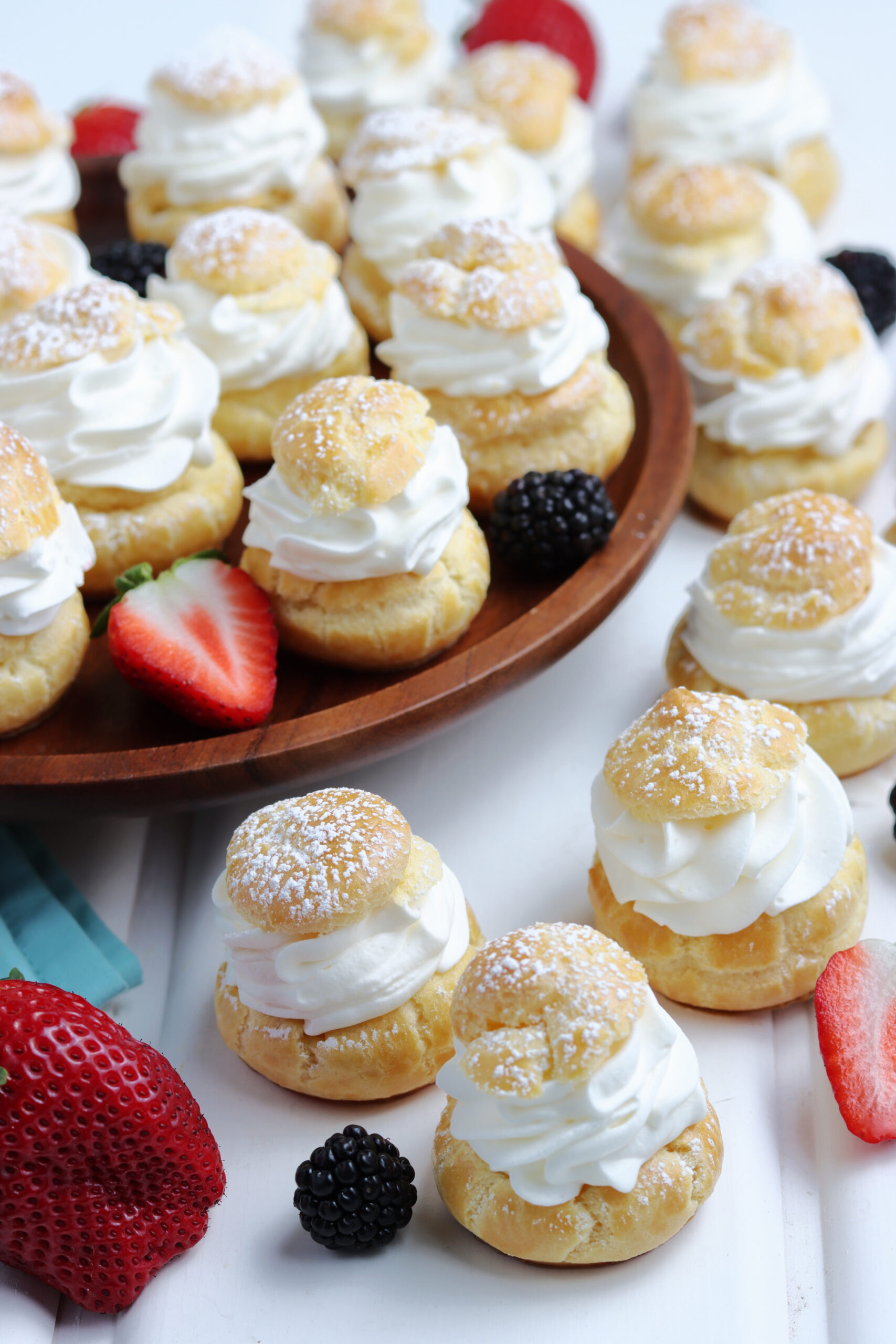 Overhead shot of Cream puffs sprinkled with powdered sugar with fresh berries in the background. 