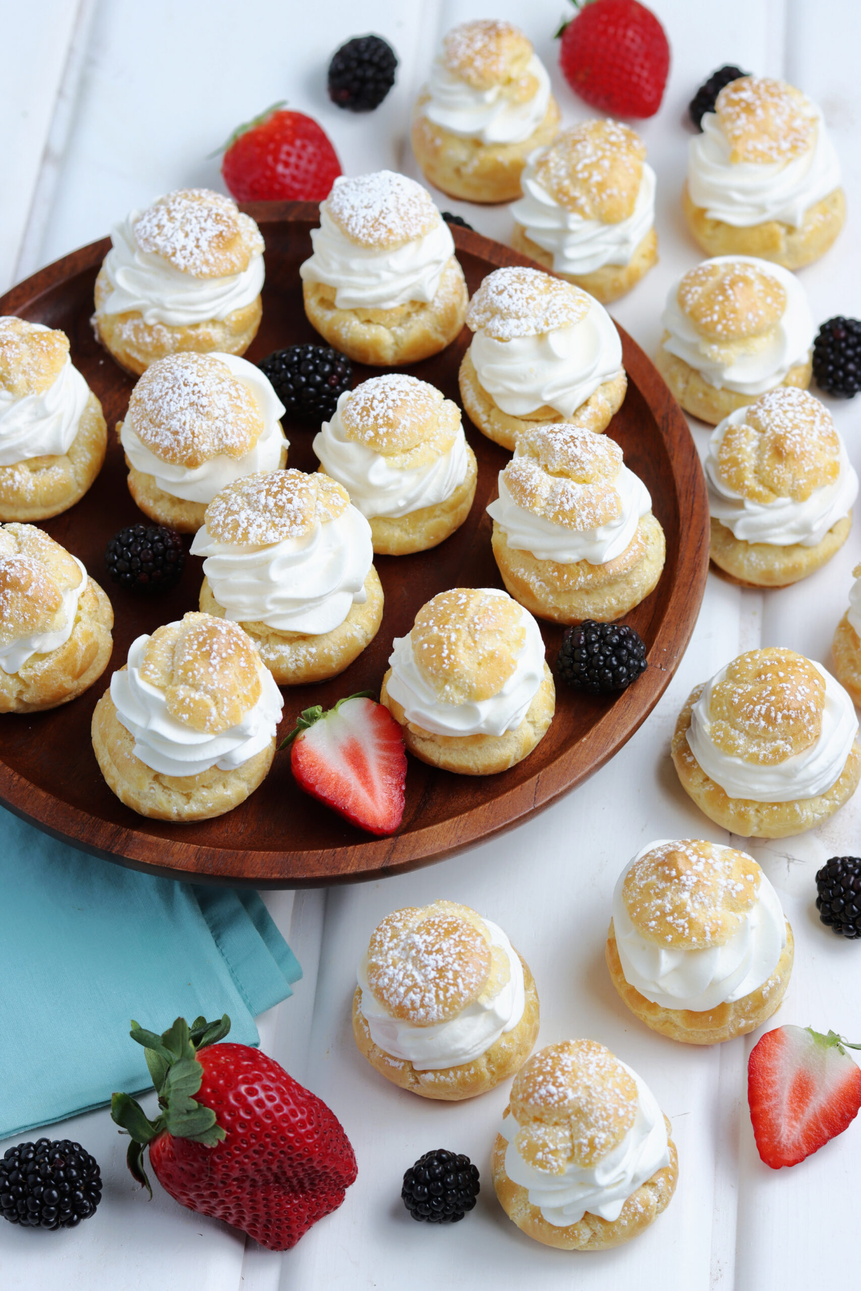 Overhead shot of Cream puffs sprinkled with powdered sugar with fresh berries in the background. 