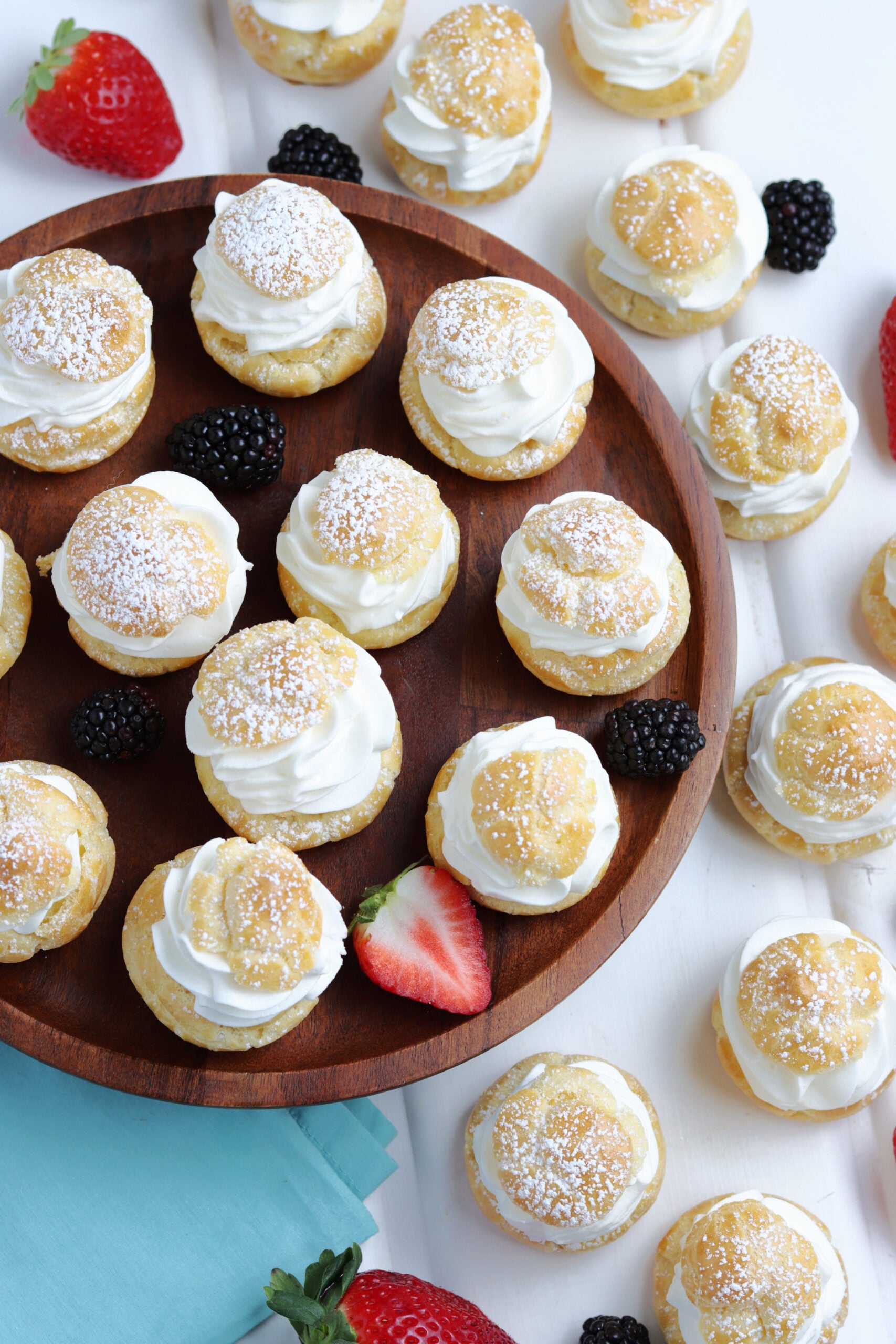 Overhead shot of Cream puffs sprinkled with powdered sugar with fresh berries in the background. 