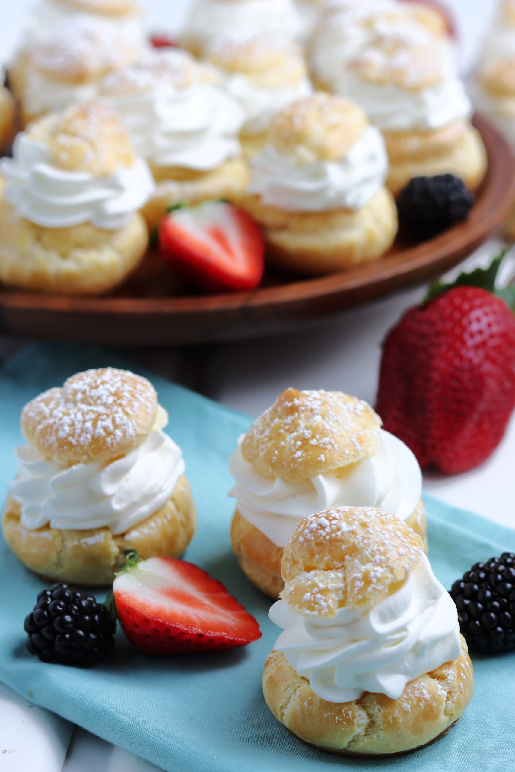 Three Cream puffs sprinkled with powdered sugar with fresh berries in the background. 