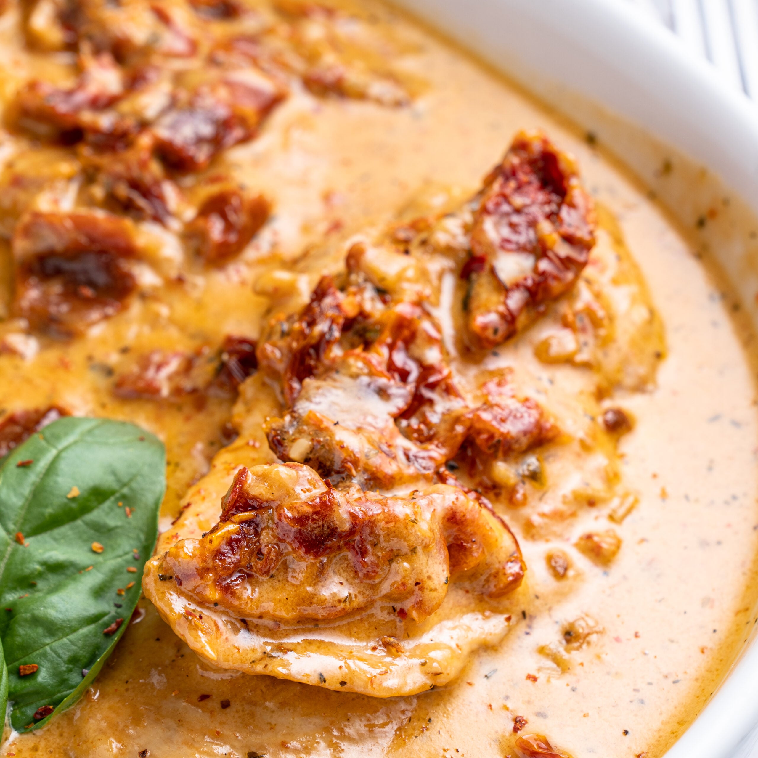Close up shot of Marry Me Chicken in a white baking dish topped with fresh basil.