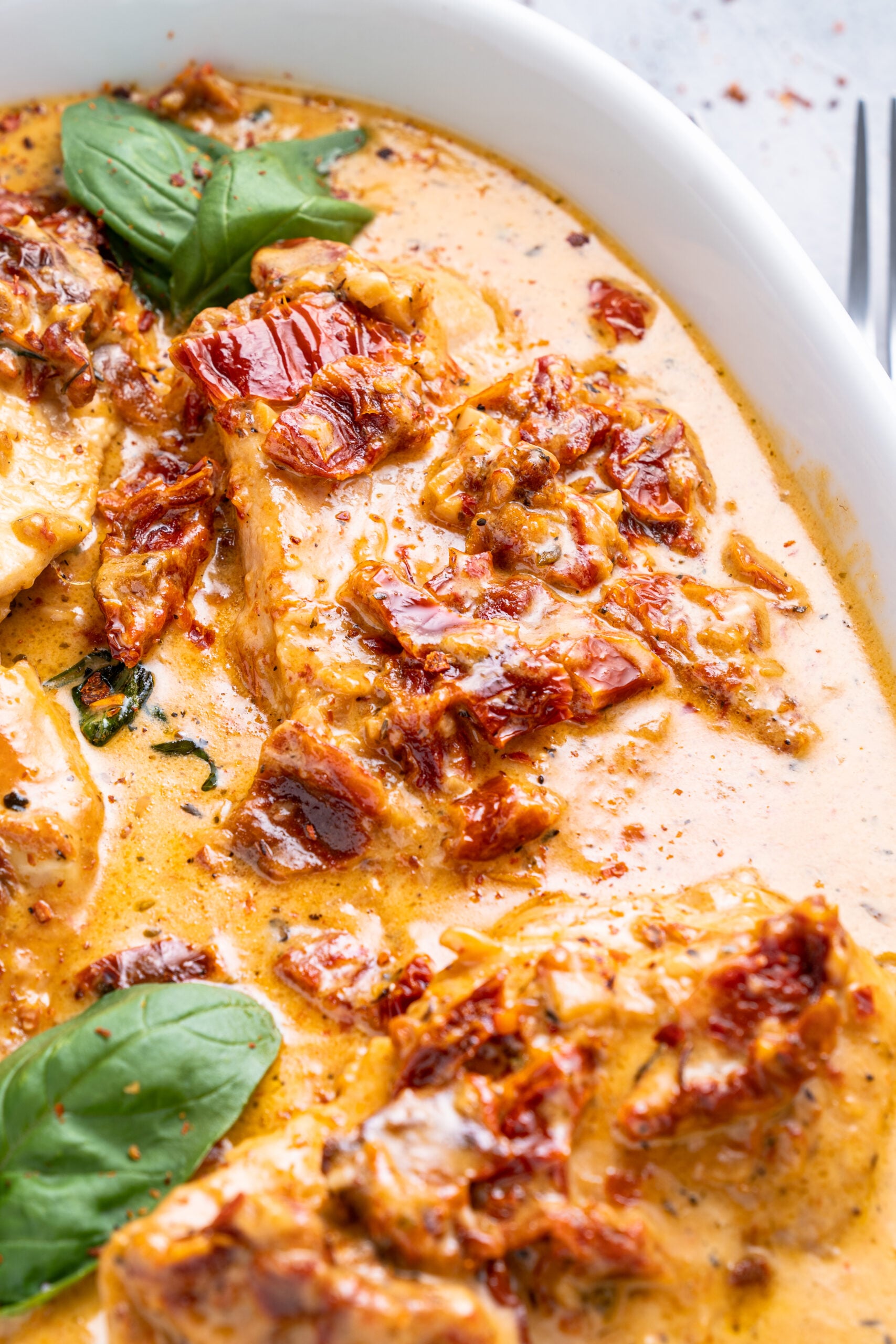 Close up shot of Marry Me Chicken in a white baking dish topped with fresh basil.