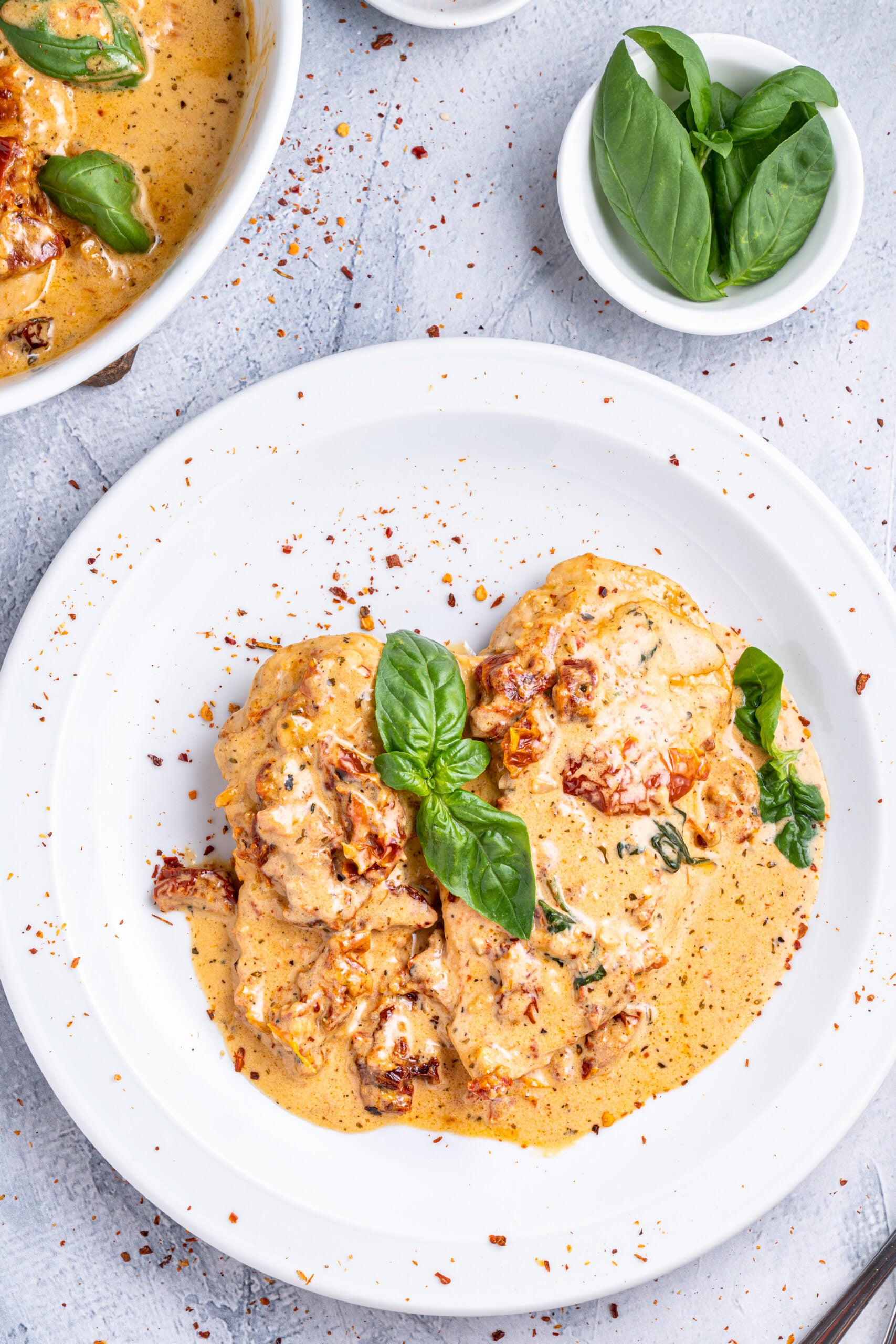 Marry Me chicken on a white plate topped with fresh basil and pepper flakes.