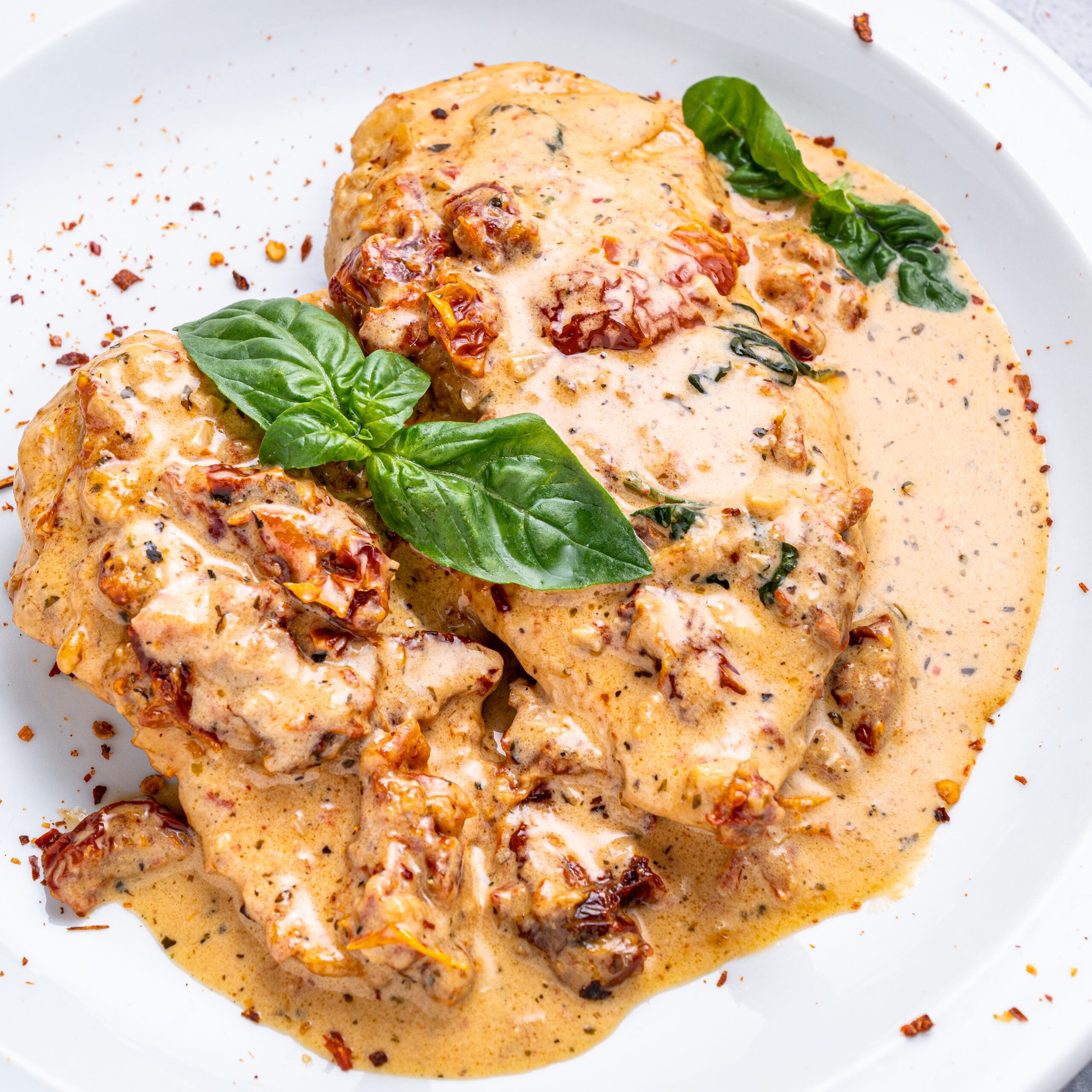 Marry Me chicken on a white plate topped with fresh basil and pepper flakes.