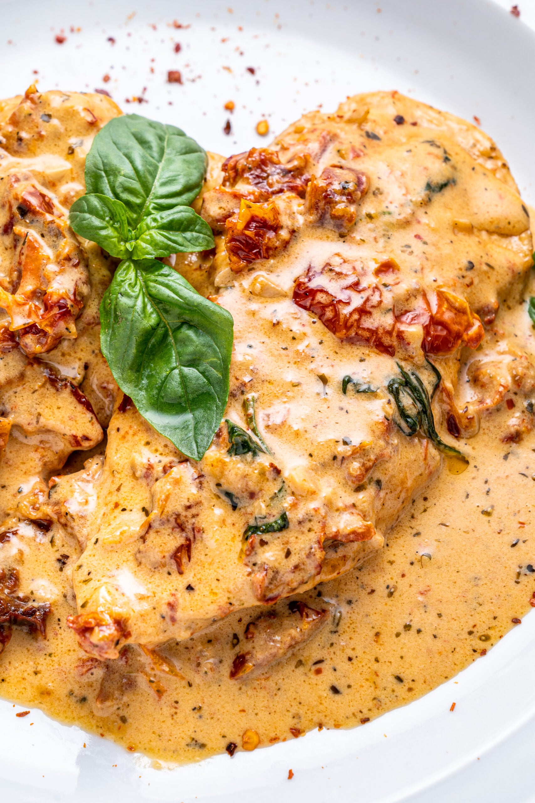 Close up shot of Marry Me chicken on a white plate topped with fresh basil and pepper flakes.