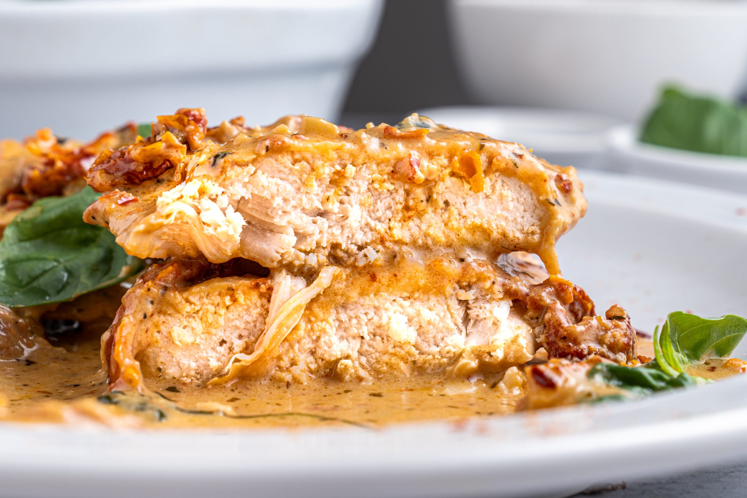 Marry Me chicken cut in half and stacked on top of each other on a white plate.