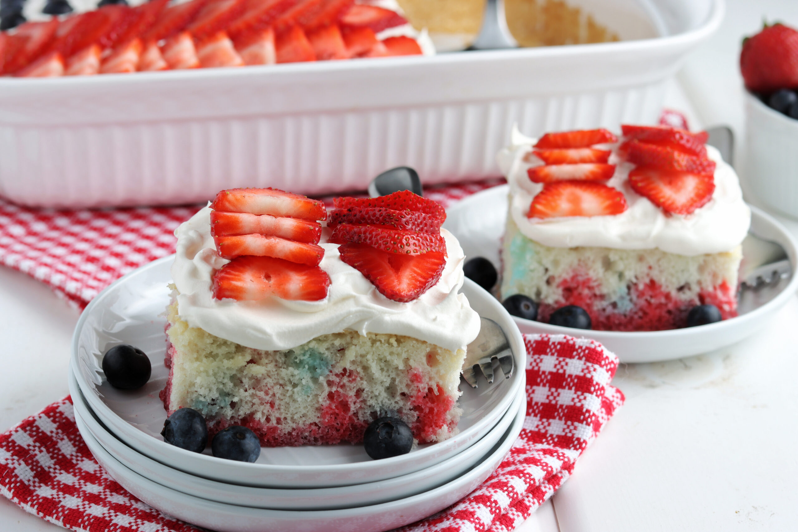Two pieces of American Flag Cake on two white plates with fresh berries.