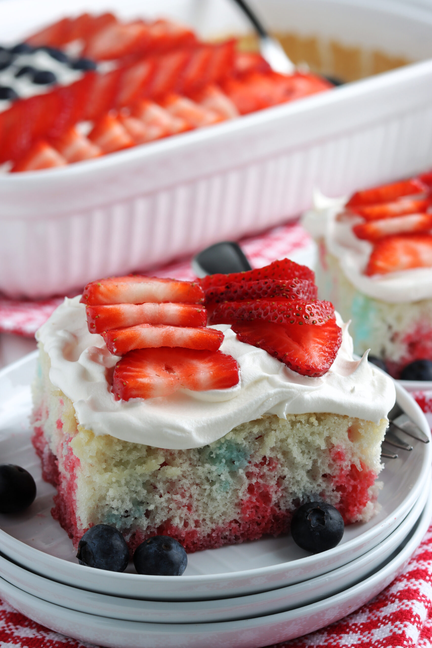 Two pieces of American Flag Cake on two white plates with fresh berries.