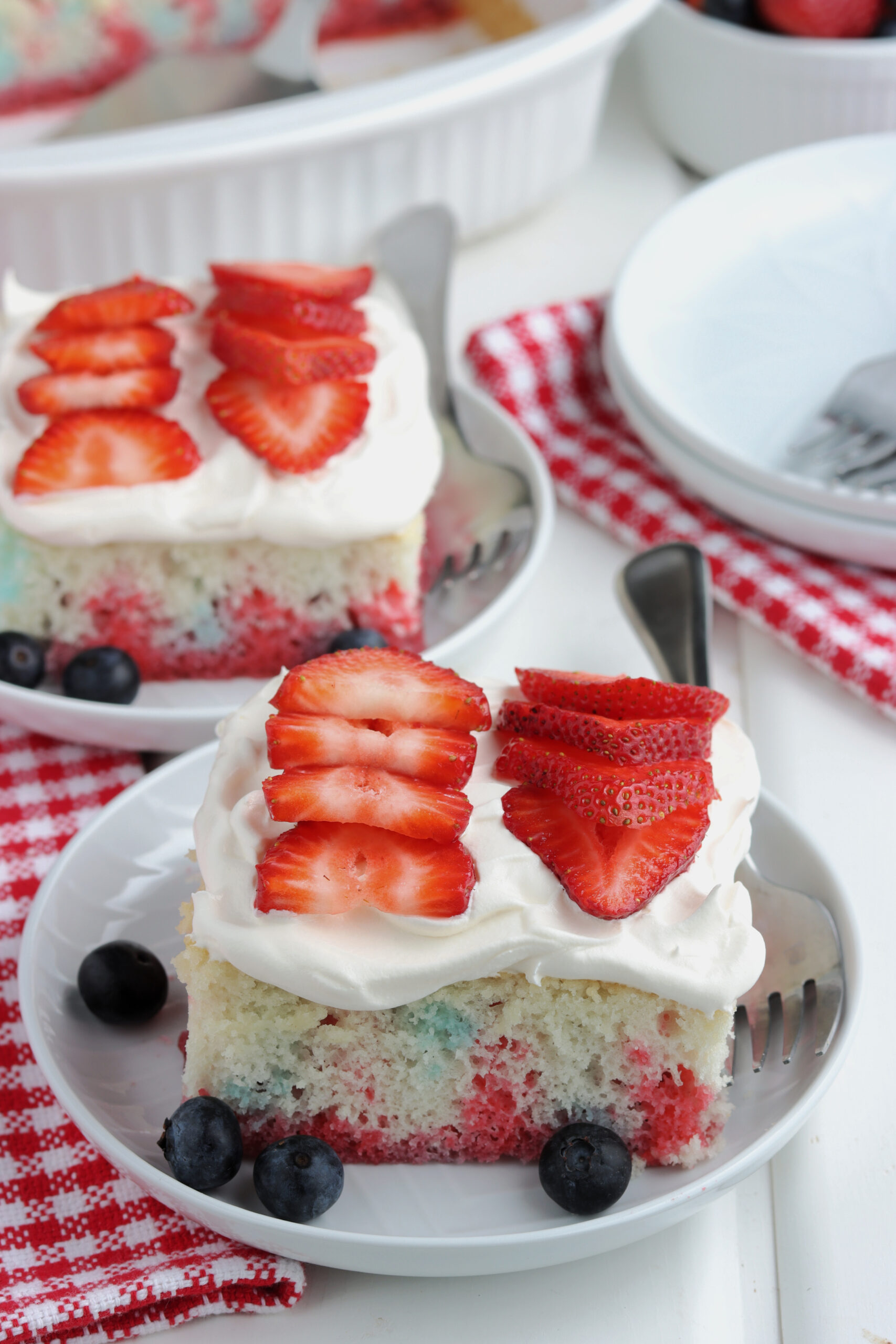 Two pieces of American Flag Cake on two white plates with fresh berries.