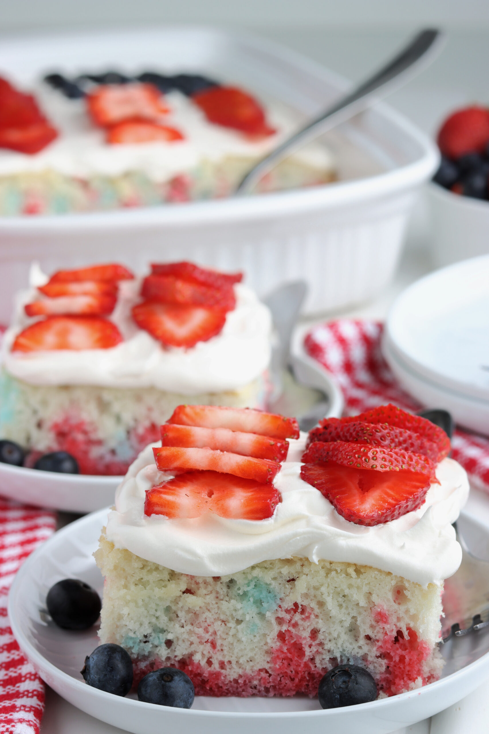 Two pieces of American Flag Cake on two white plates with fresh berries.