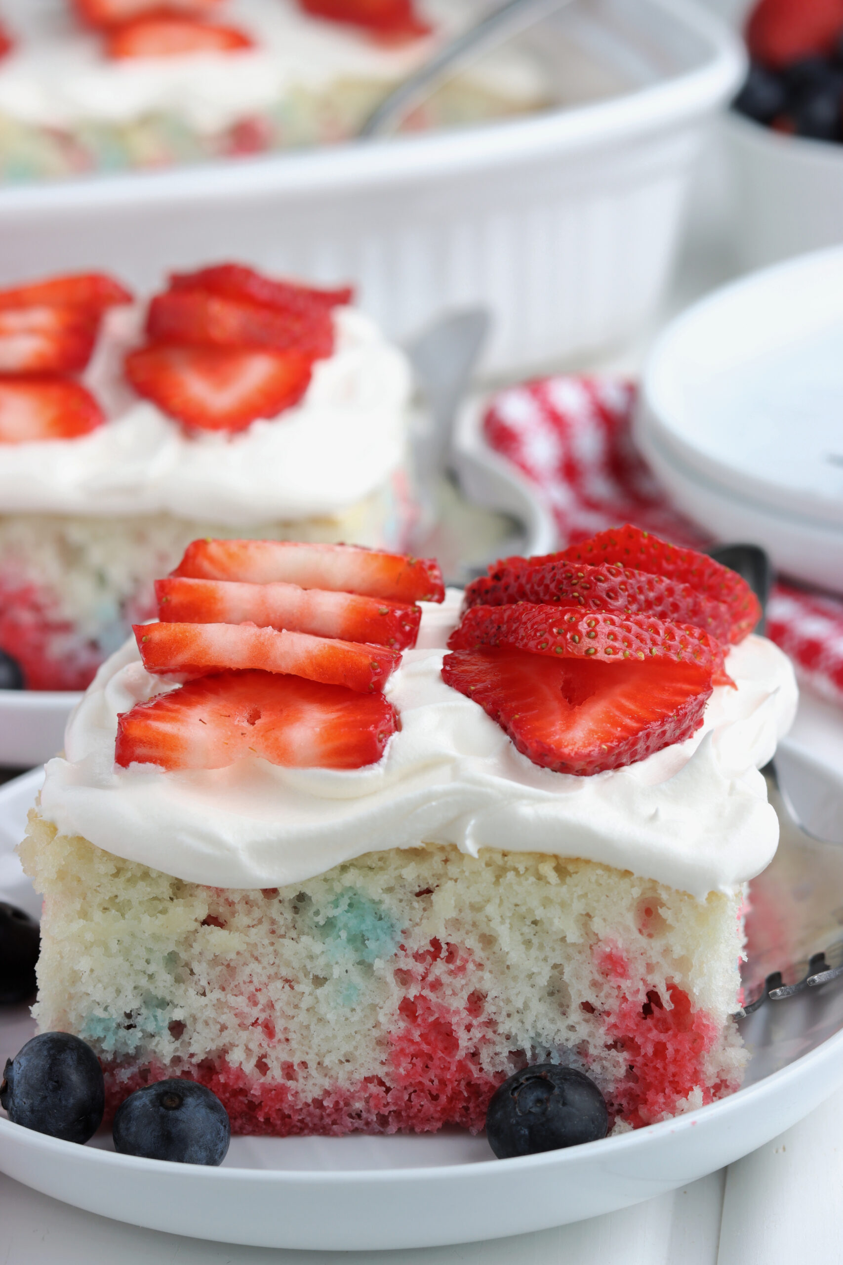 Two pieces of American Flag Cake on two white plates with fresh berries.