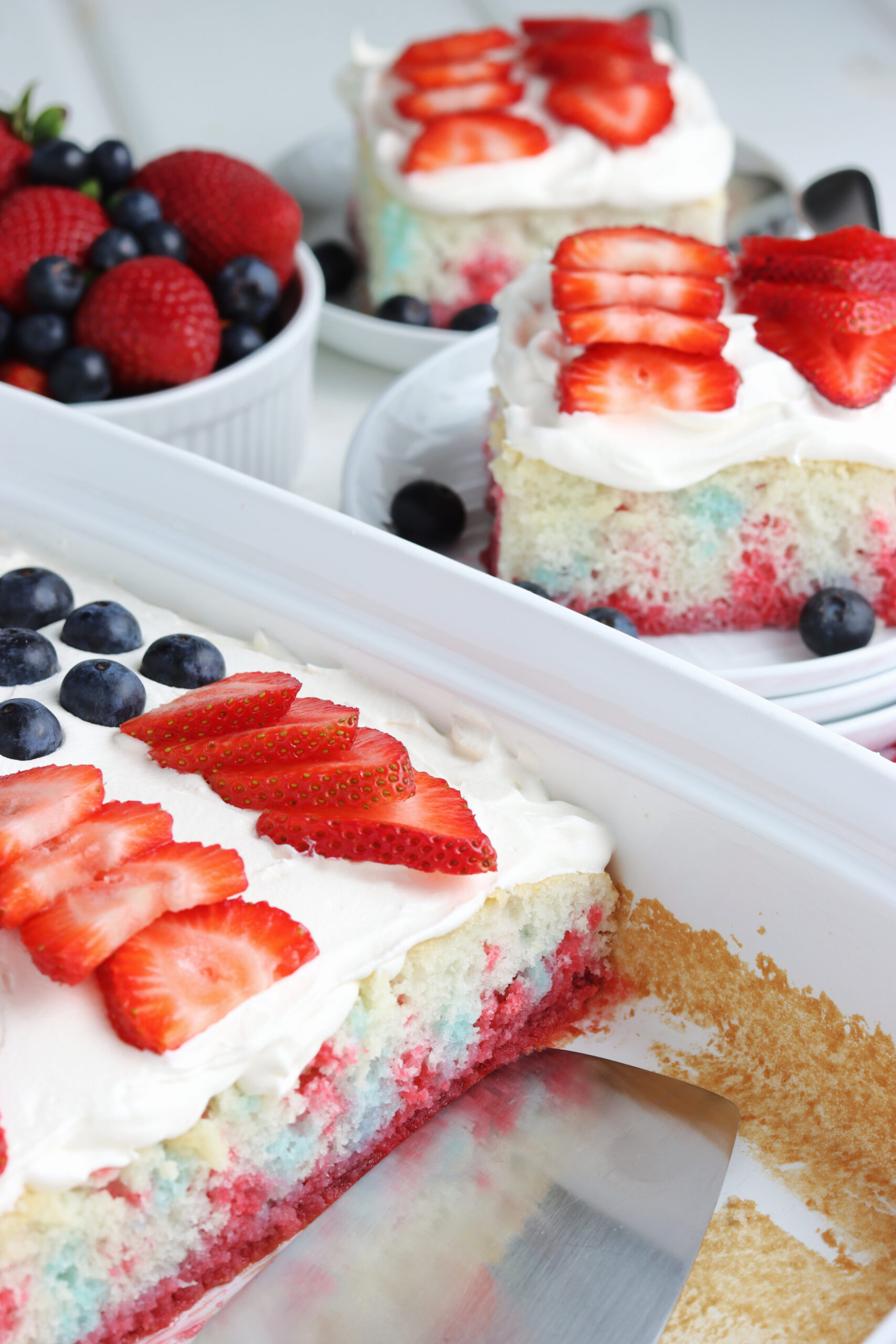 Two pieces of American Flag Cake on two white plates with fresh berries.