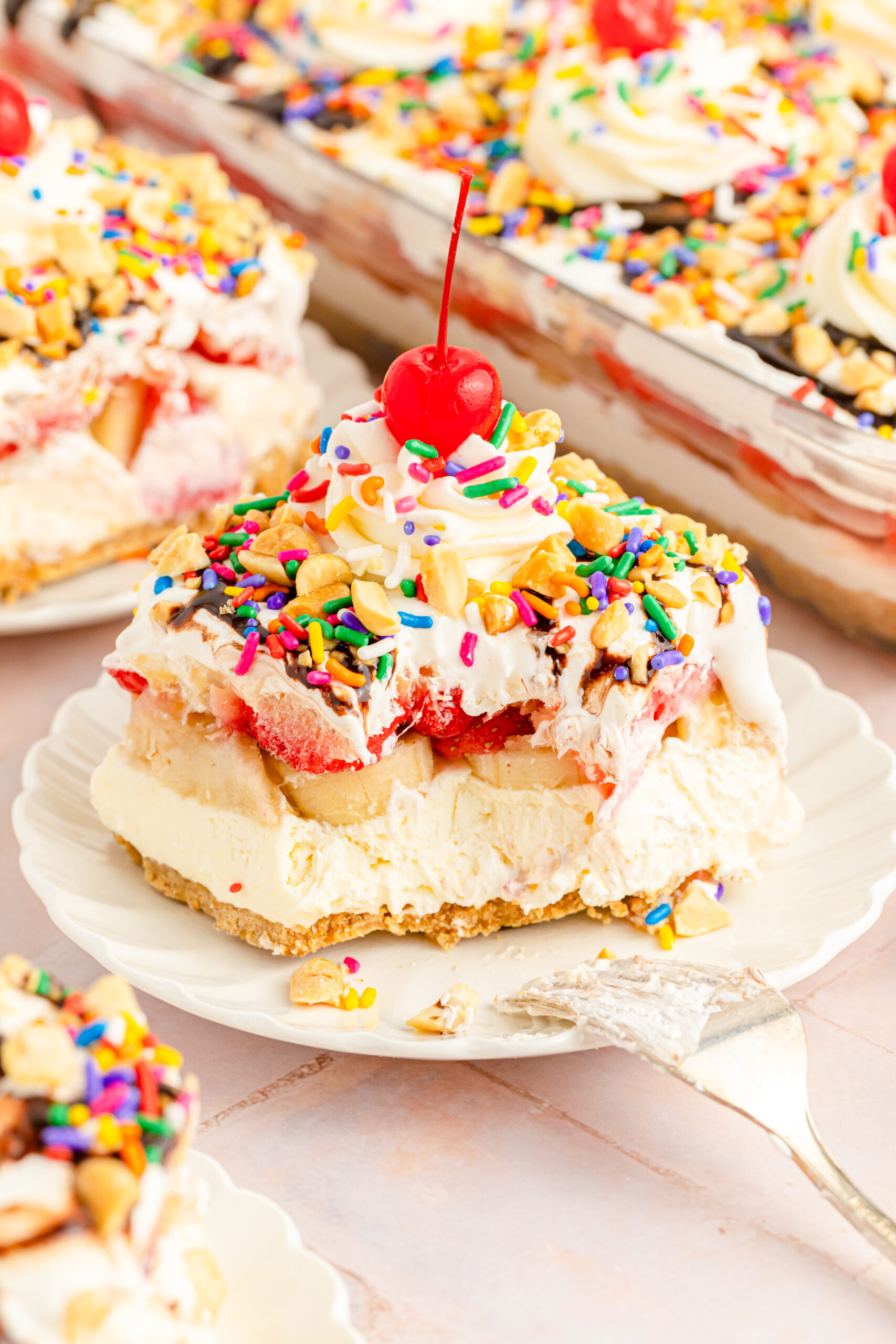 Front view of a slice of No Bake Banana Split Cake on a white plate with a bite removed by a silver fork.
