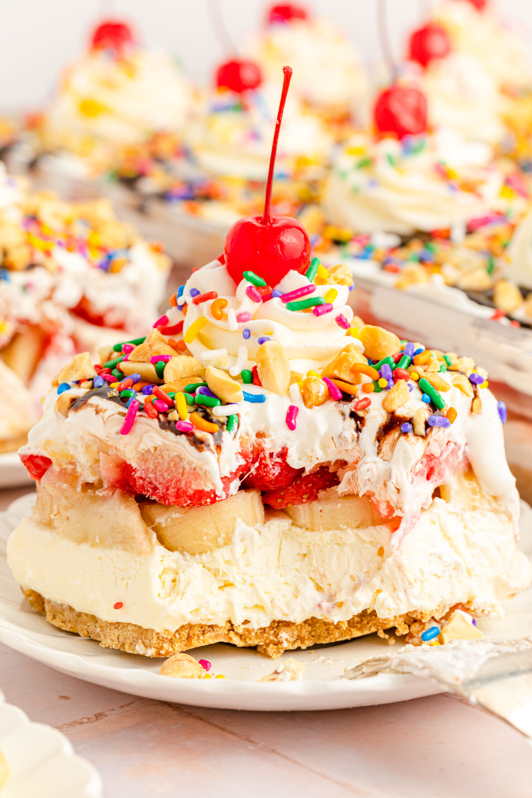 Close up view of a slice of No Bake Banana Split Cake on a white plate with a bite removed by a silver fork.
