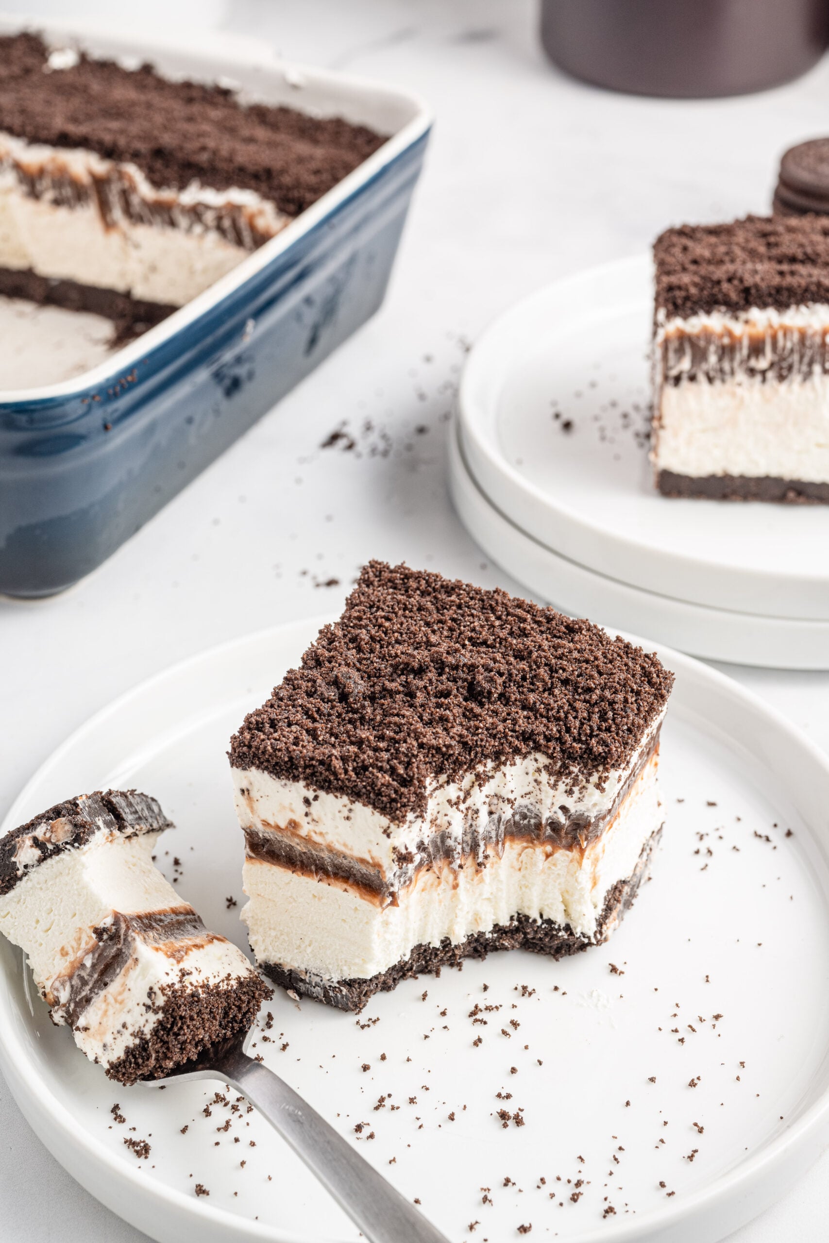 Overhead view of a slice of Oreo Delight on a white plate with a bite removed by a silver fork.