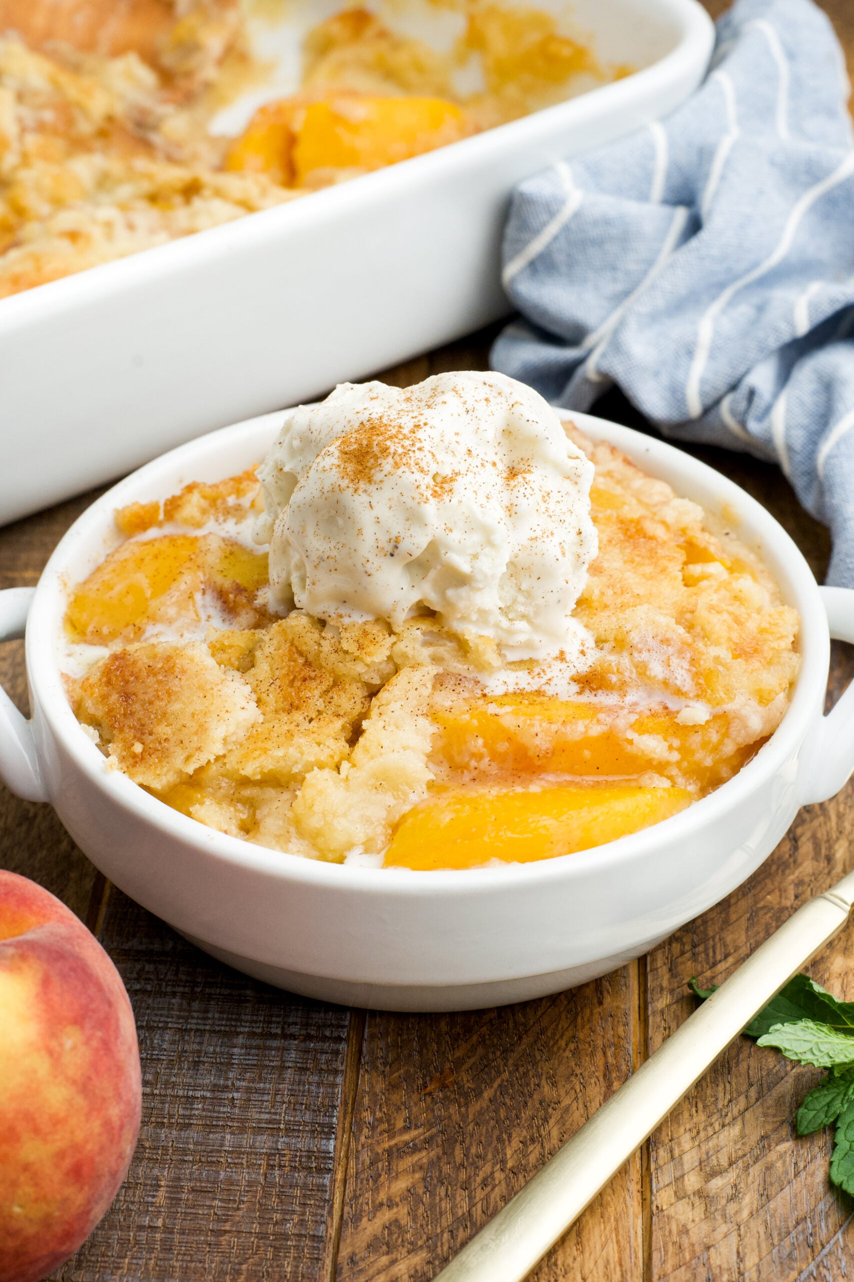 Front view of a serving of Peach Dump Cake in a white bowl topped with a scoop of vanilla ice cream.