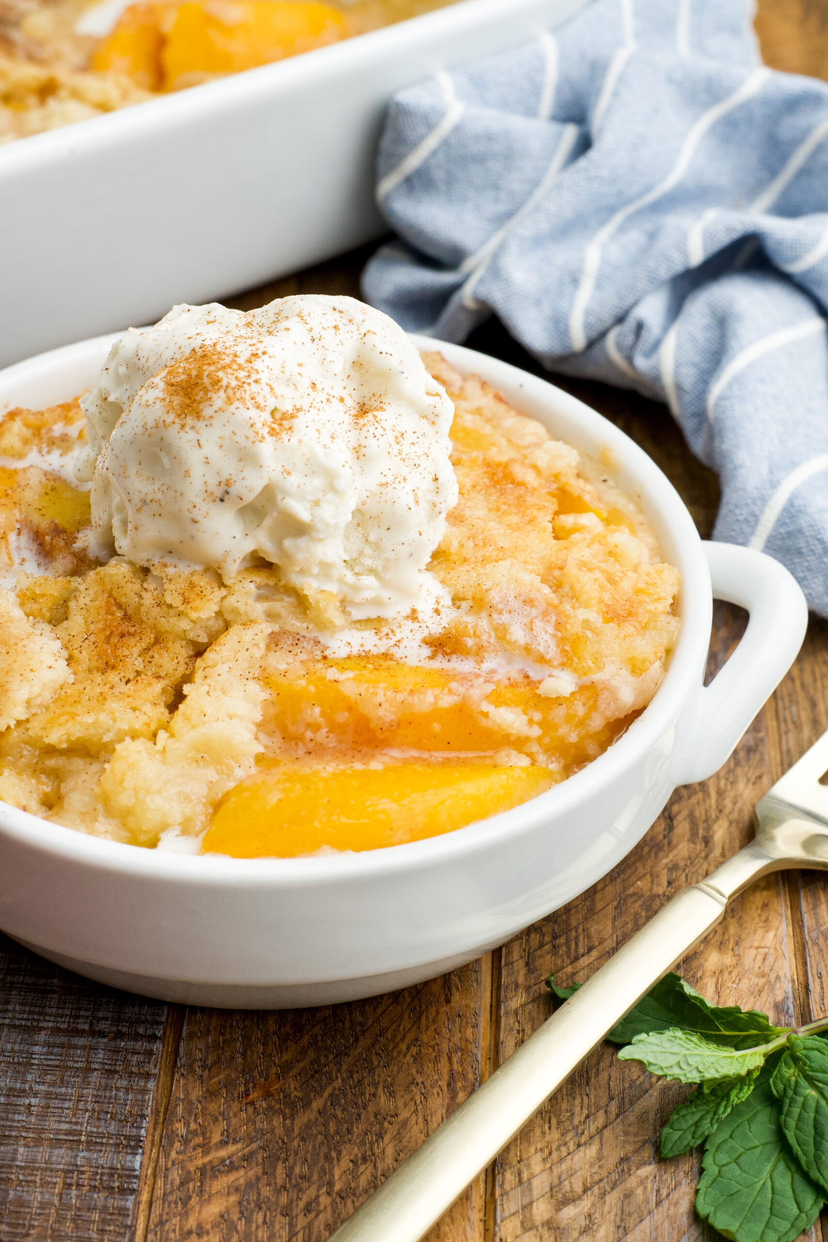 Front view of a serving of Peach Dump Cake in a white bowl topped with a scoop of vanilla ice cream.