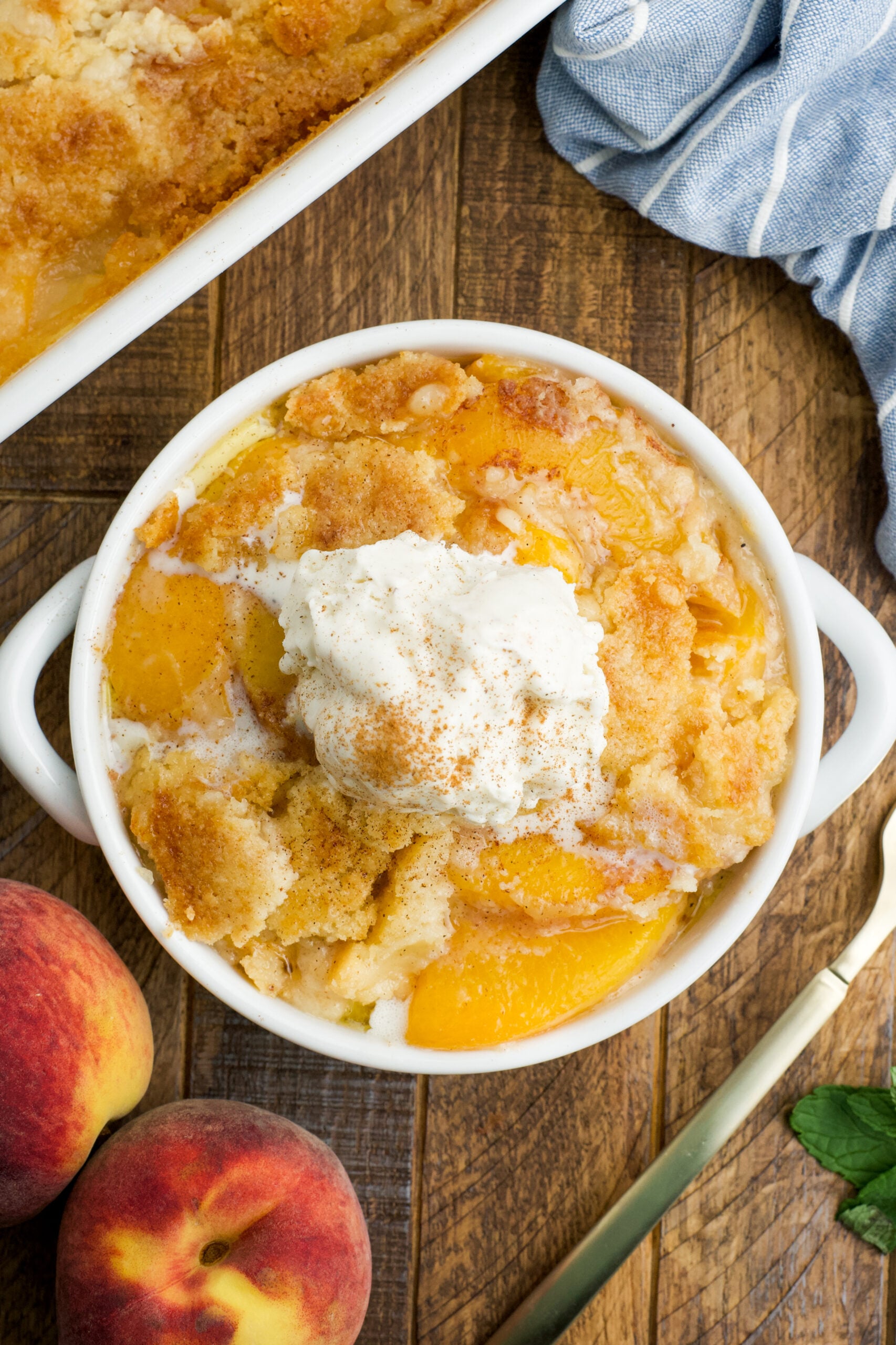 Overhead view of a serving of Peach Dump Cake in a white bowl topped with a scoop of vanilla ice cream.